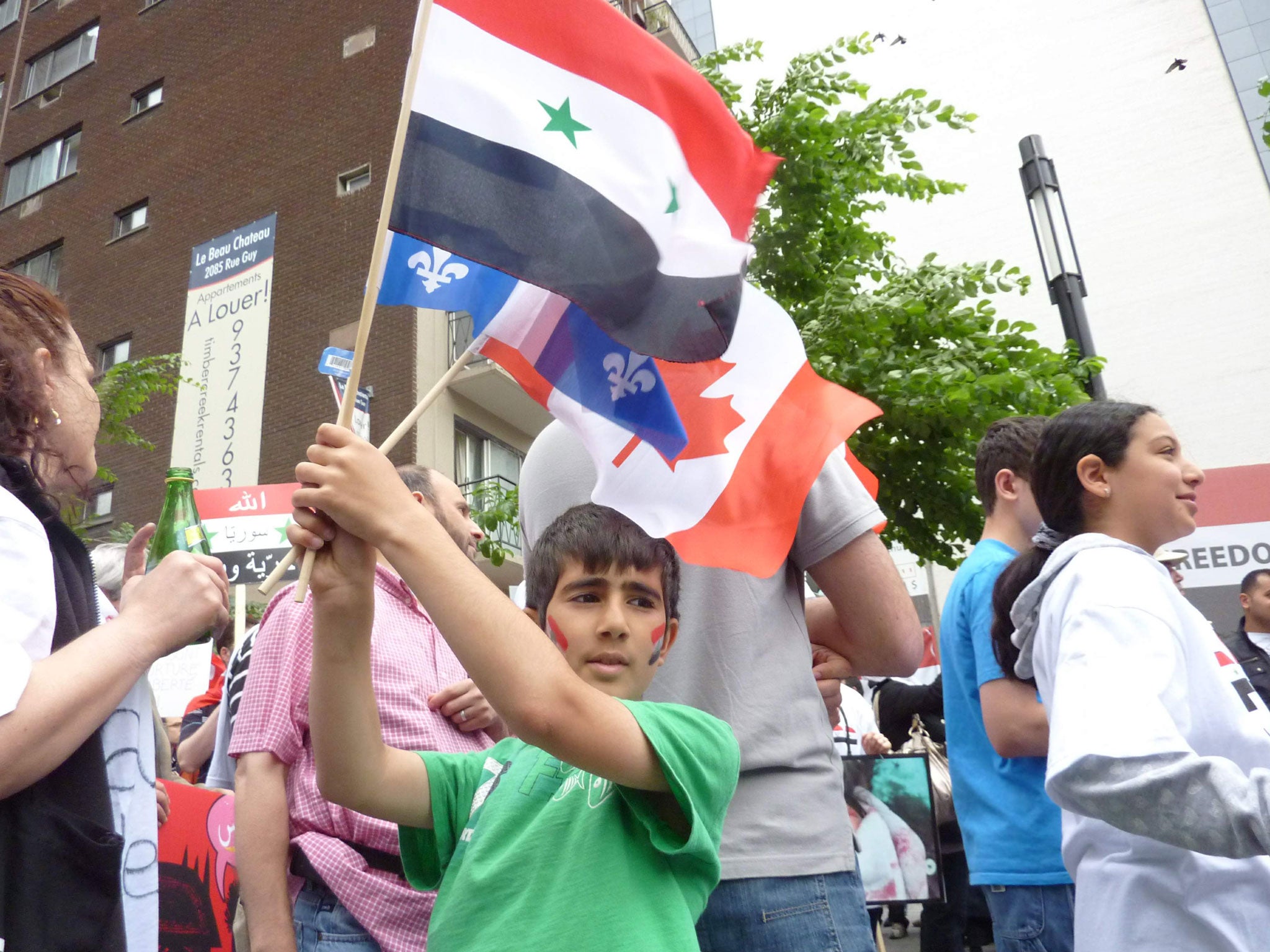 A young boy holds 3 flags, Syrian (with stars), Canadian (red) and Quebec (blue), in a demo against Syrian president Bashar al-Assad. Montreal, Quebec, Canada. June 11, 2011.