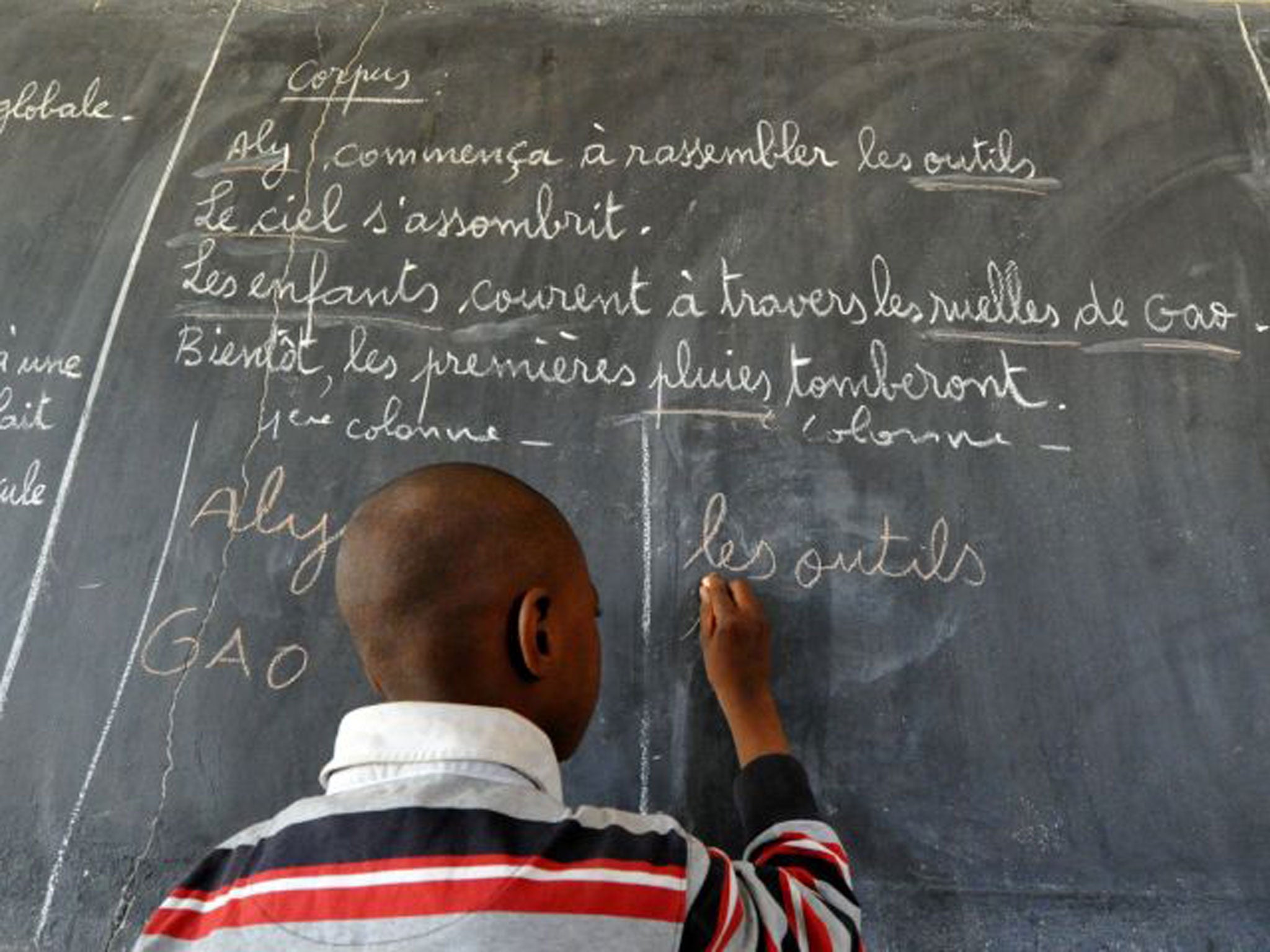 A child writes in French on a classic classroom blackboard