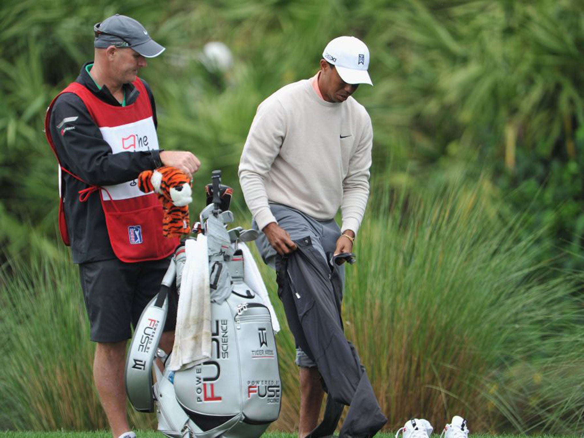 Tiger Woods pulls on his rain pants after removing his shoes at the sixth yesterday