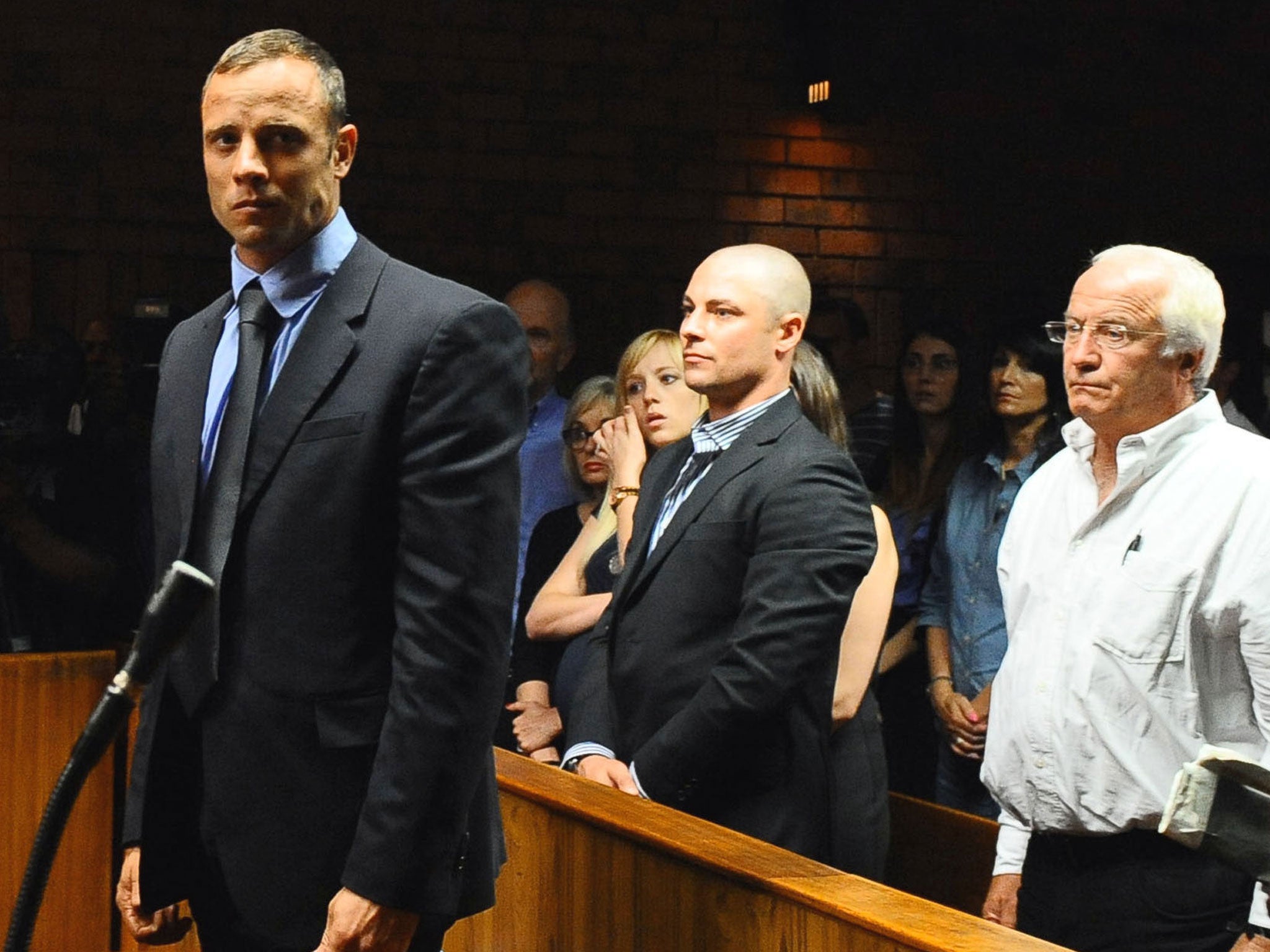 Olympian Oscar Pistorius stands following his bail hearing, as his brother Carl, centre, and father Henke look on
