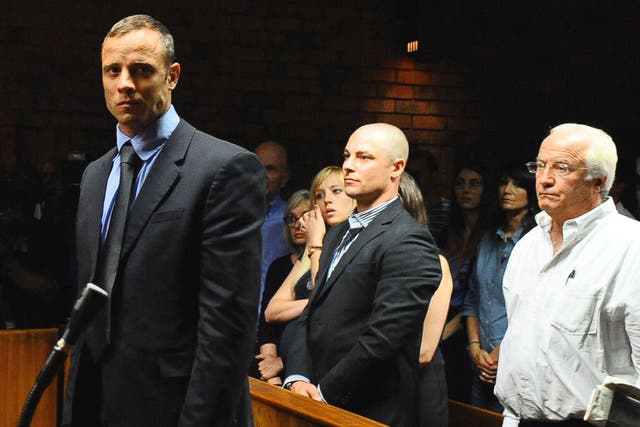 Olympian Oscar Pistorius stands following his bail hearing, as his brother Carl, centre, and father Henke look on