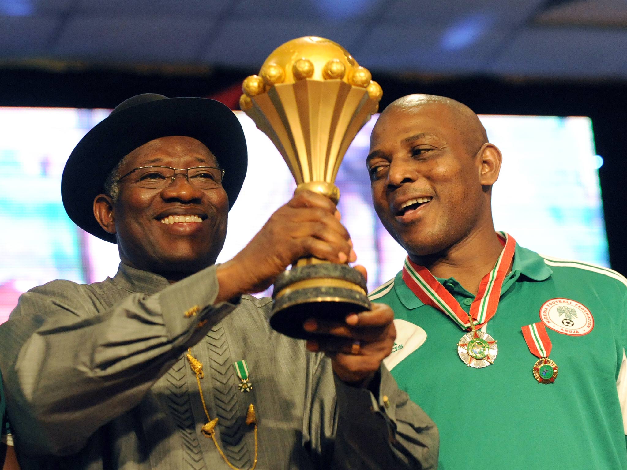 Coach of the mens Nigerian football team Stephen Keshi looks on as President Goodluck Jonathan raises the trophy won at the 2013 African Cup of Nations