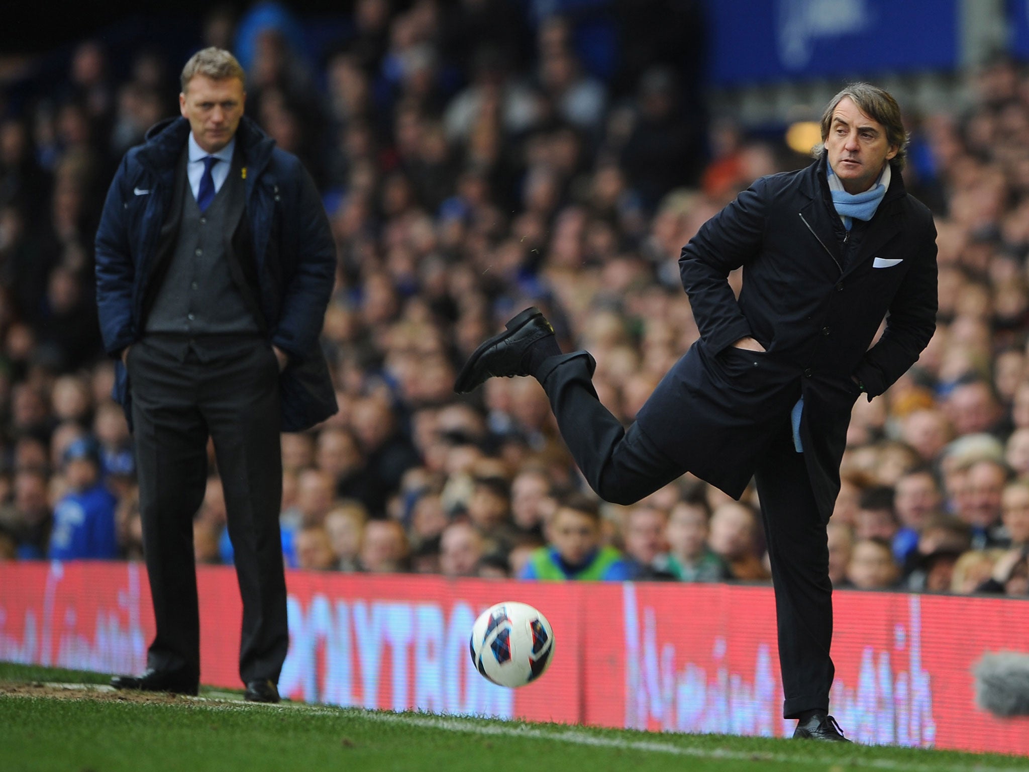 Manchester City Manager Roberto Mancini controls the ball as Everton Manager David Moyes looks on