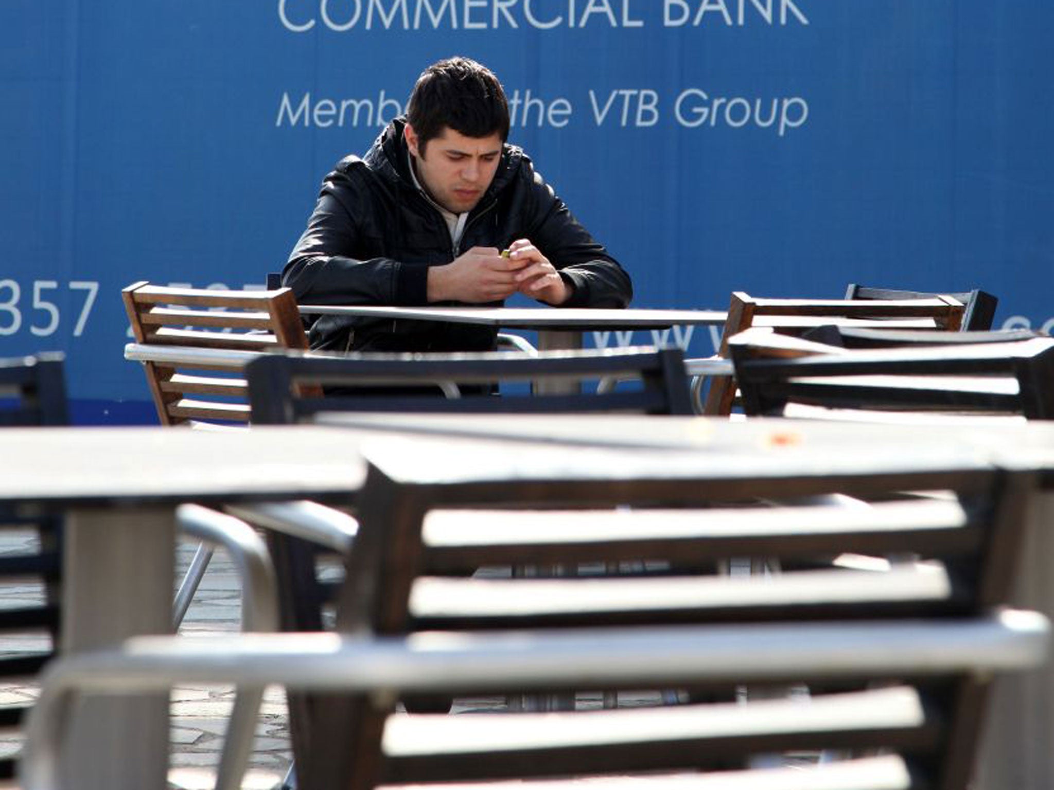 A man sits next to a billboard for a Russian bank in the Mediterranean city of in Limassol