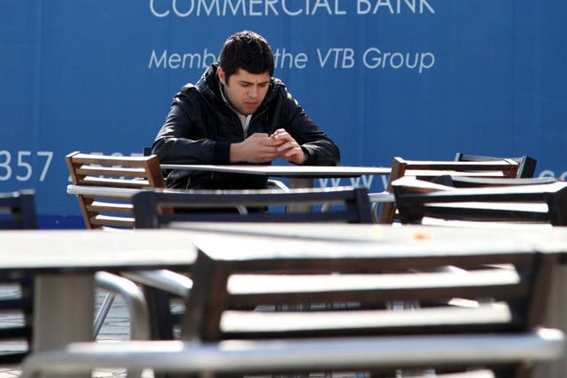 A man sits next to a billboard for a Russian bank in the Mediterranean city of in Limassol