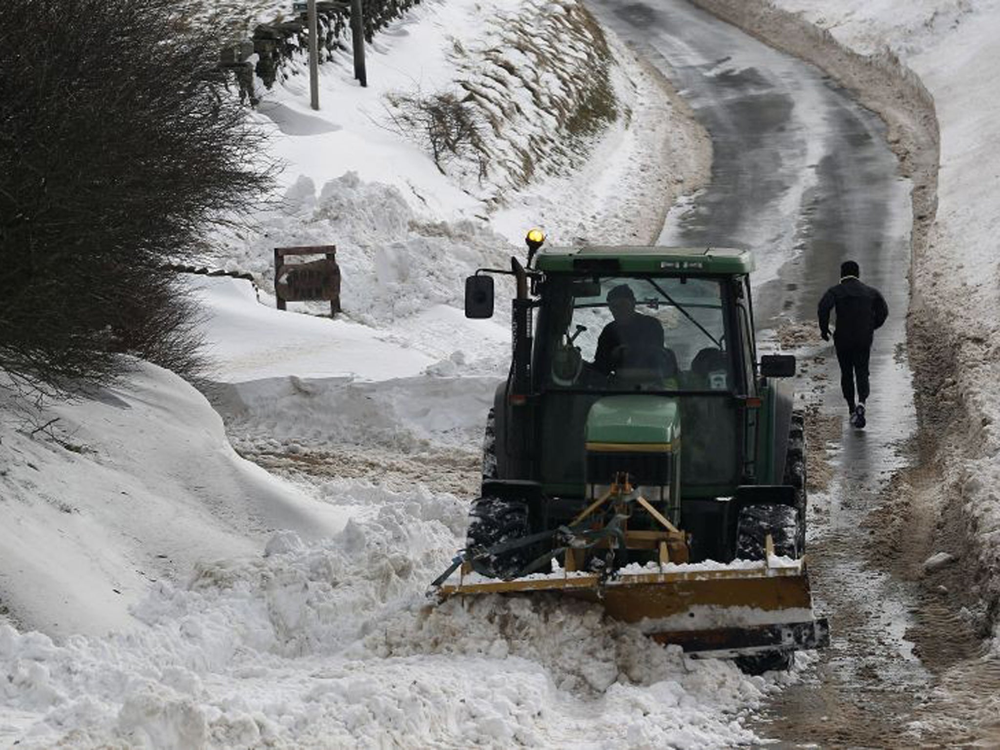 A runner makes his way up a cleared road flanked by deep snow in Burnley