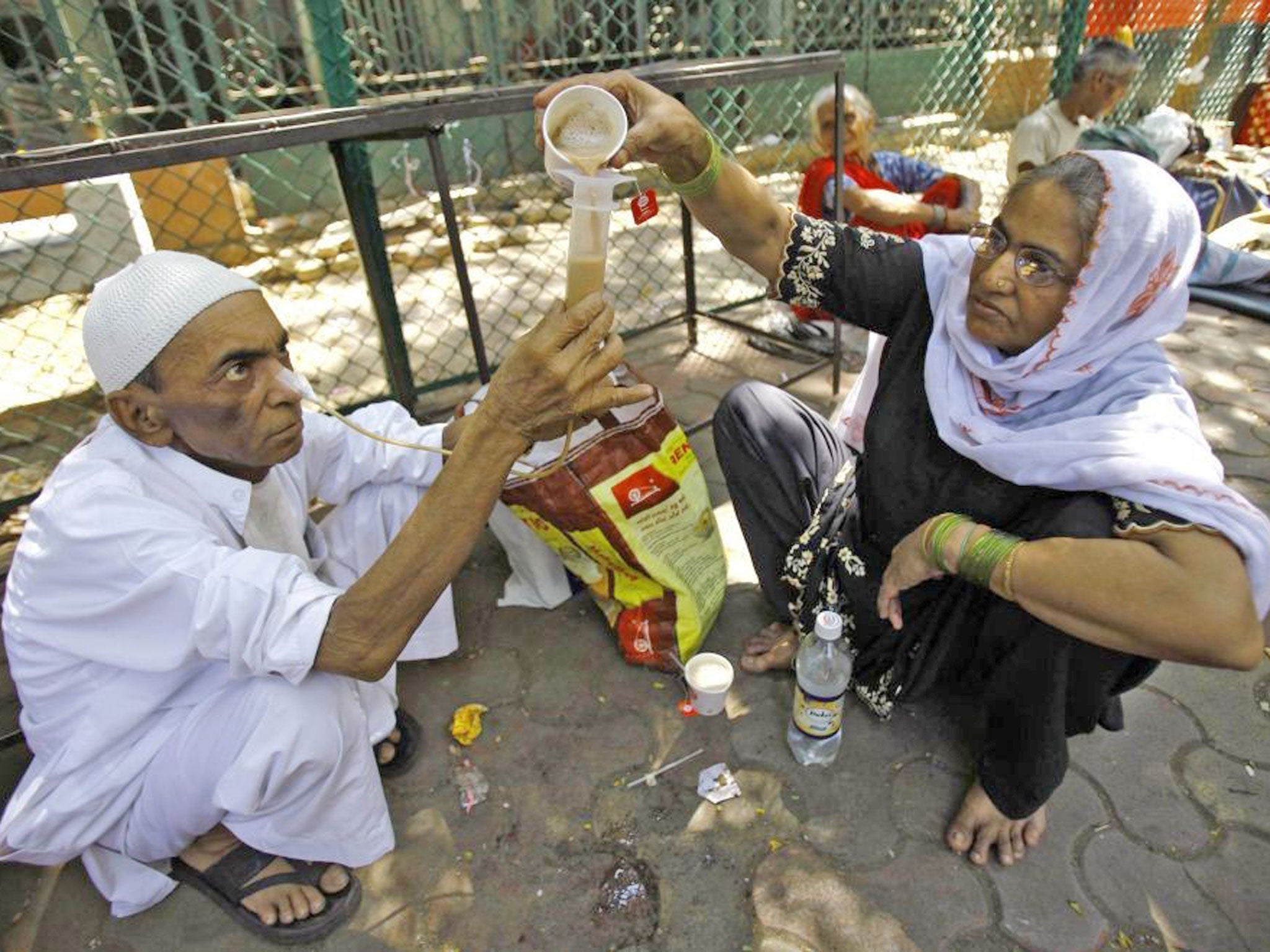 Kamal Ahmad, 68, who is suffering from throat cancer, gets help from a relative to drink tea through his nose outside Tata cancer hospital in Mumbai, India