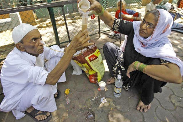 Kamal Ahmad, 68, who is suffering from throat cancer, gets help from a relative to drink tea through his nose outside Tata cancer hospital in Mumbai, India