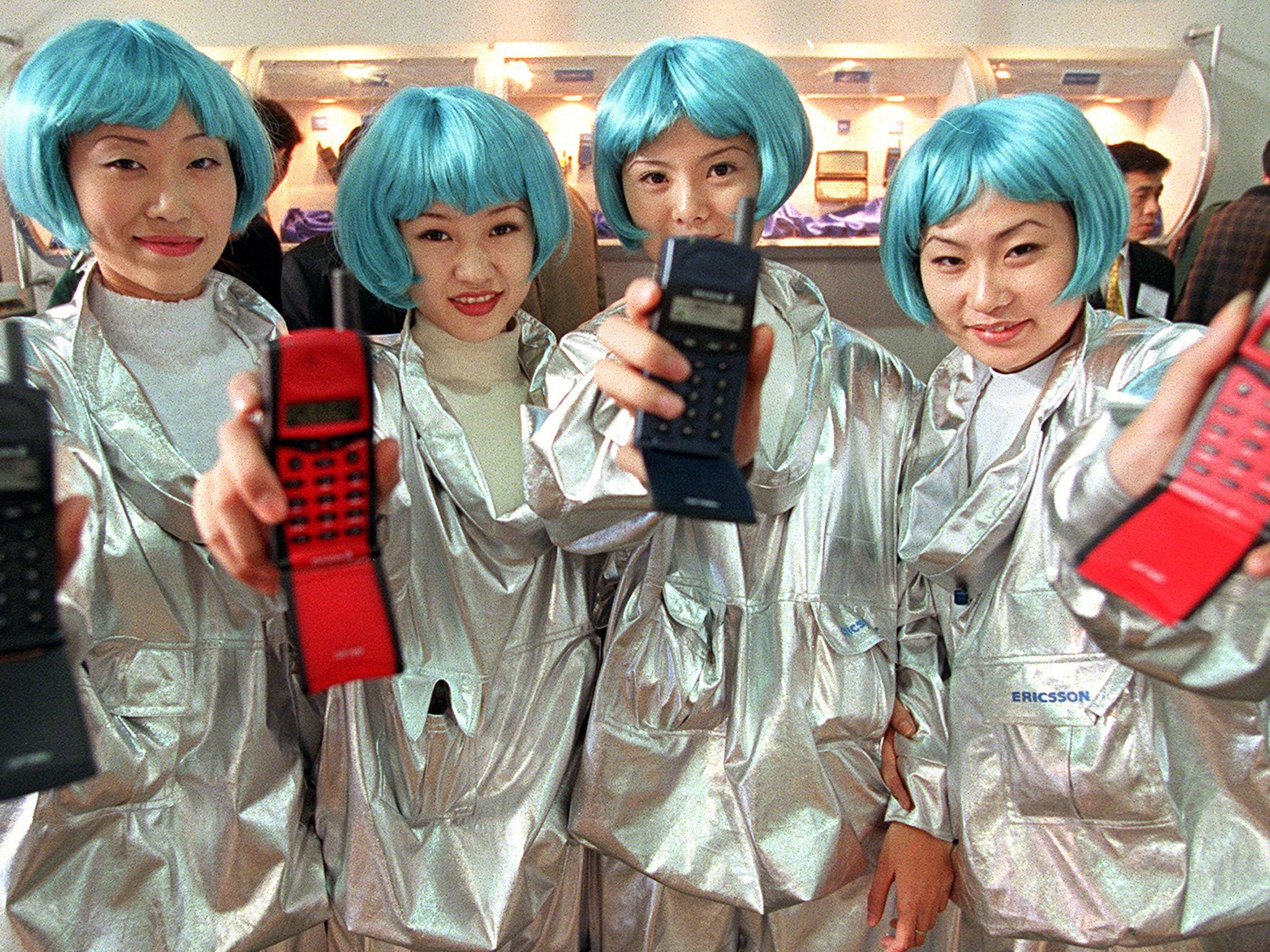 Four Chinese women, wearing blue wigs, display their company's latest mobile phones 27 October during China's international telecommuncations equipement and technology exhibition in Beijing