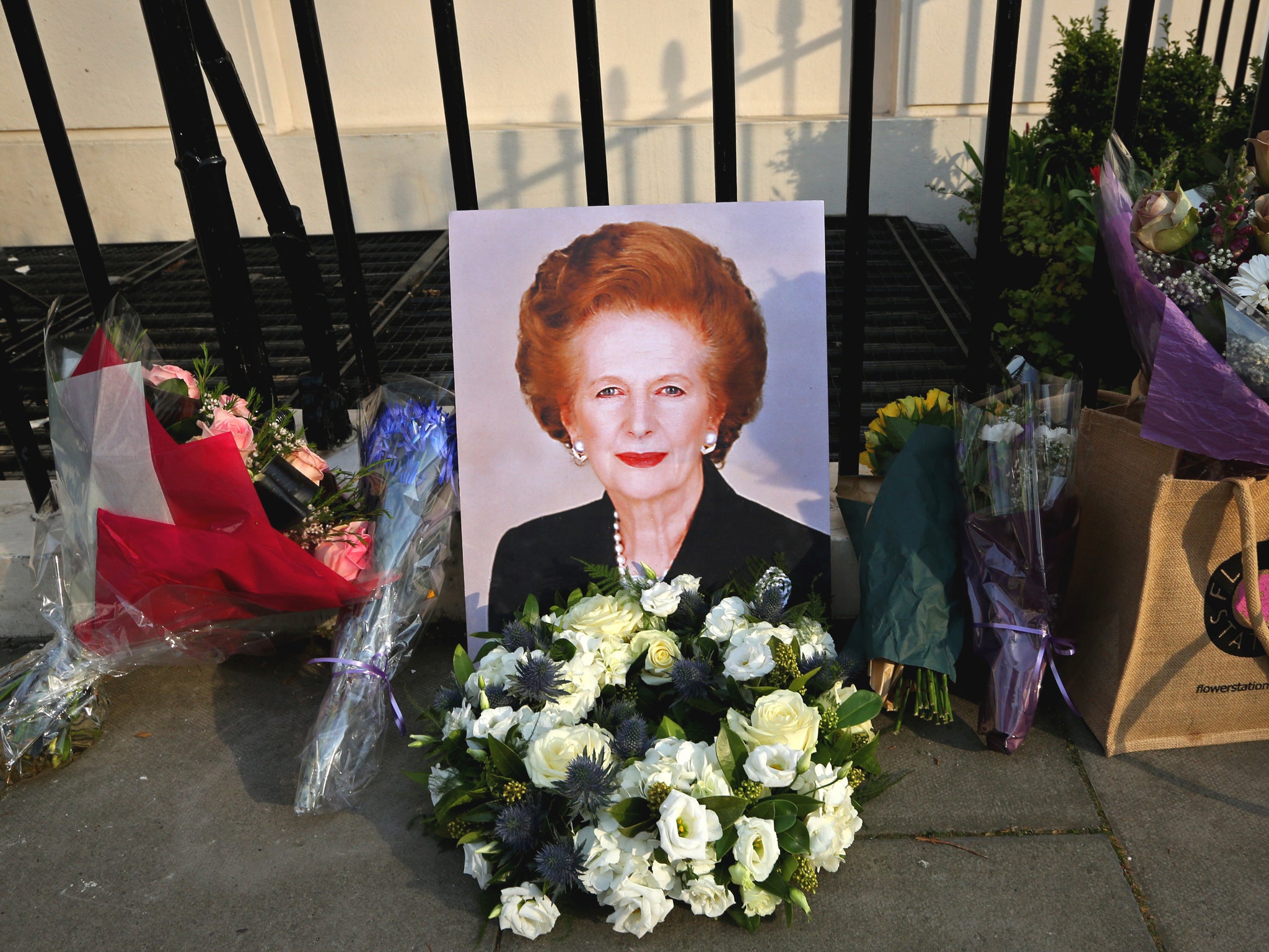 A portrait of former Prime Minister Margaret Thatcher is left next to floral tributes outside her residence