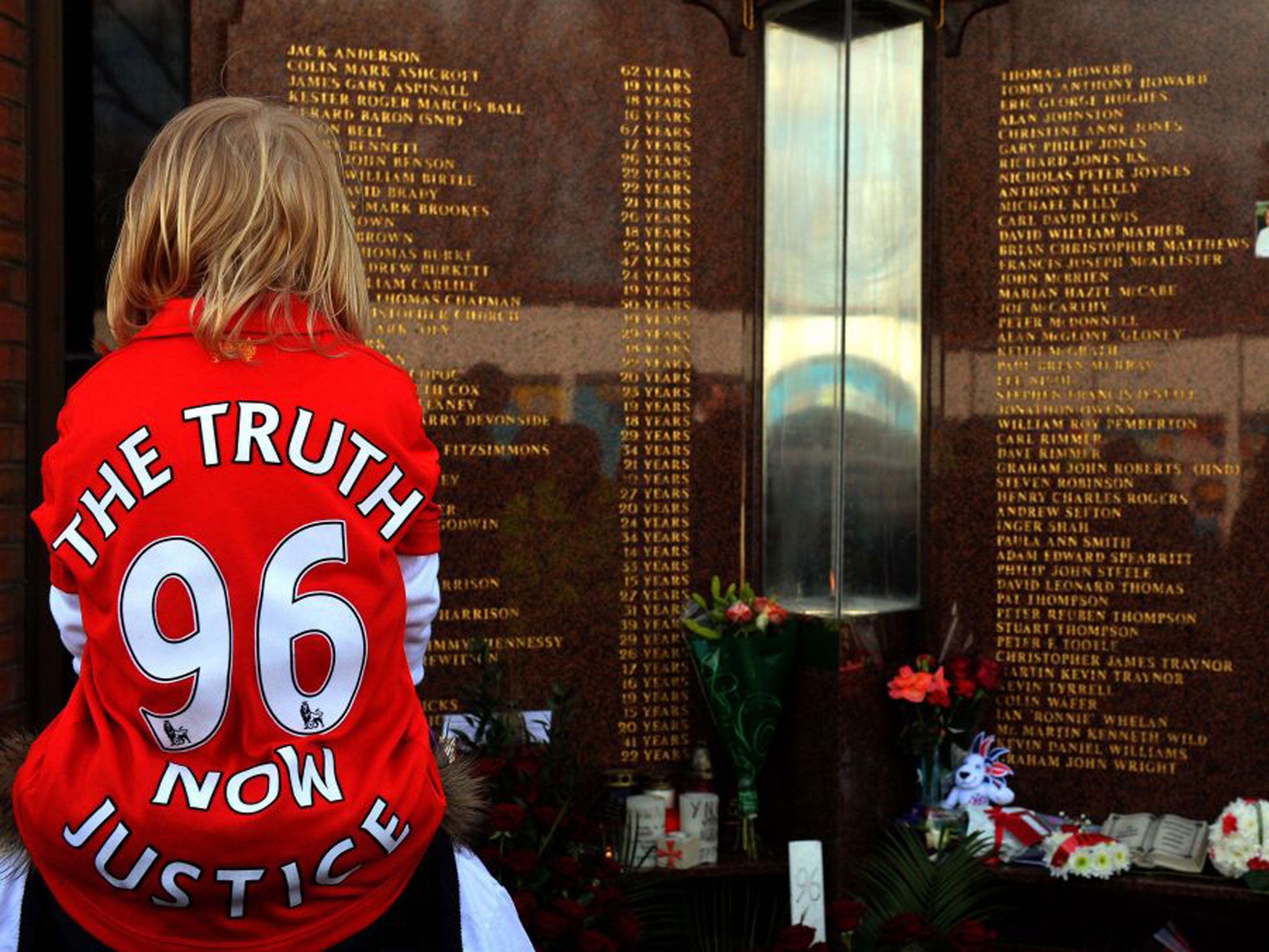 A child wears a Jersey bearing the writing "Justice for the 96" in front of the Hillsborough Memorial at Liverpool FC's Anfield football ground