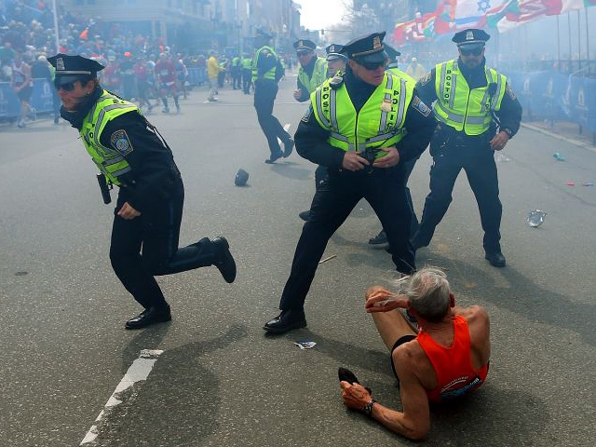 Bill Iffrig, 78, lies on the ground as police officers react to a second explosion at the finish line of the Boston Marathon