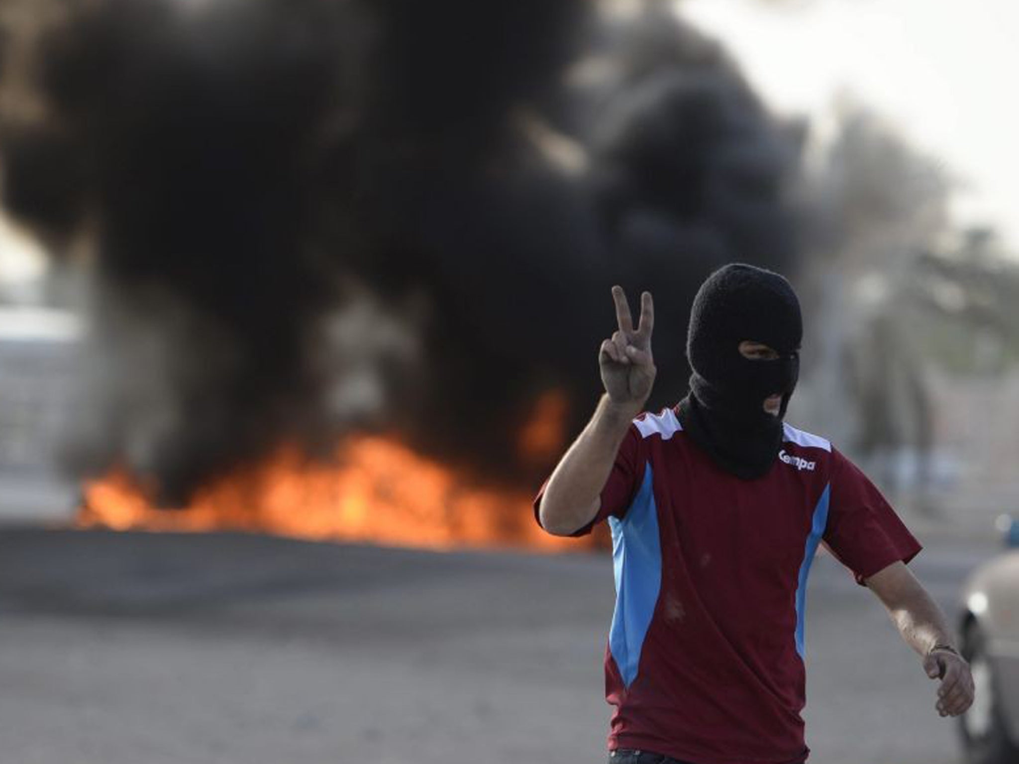 An anti-F1 protester flash the 'V' sign after setting tyres on fire to block a road in Sanabis village, on the outskirts of the Bahraini capital Manama