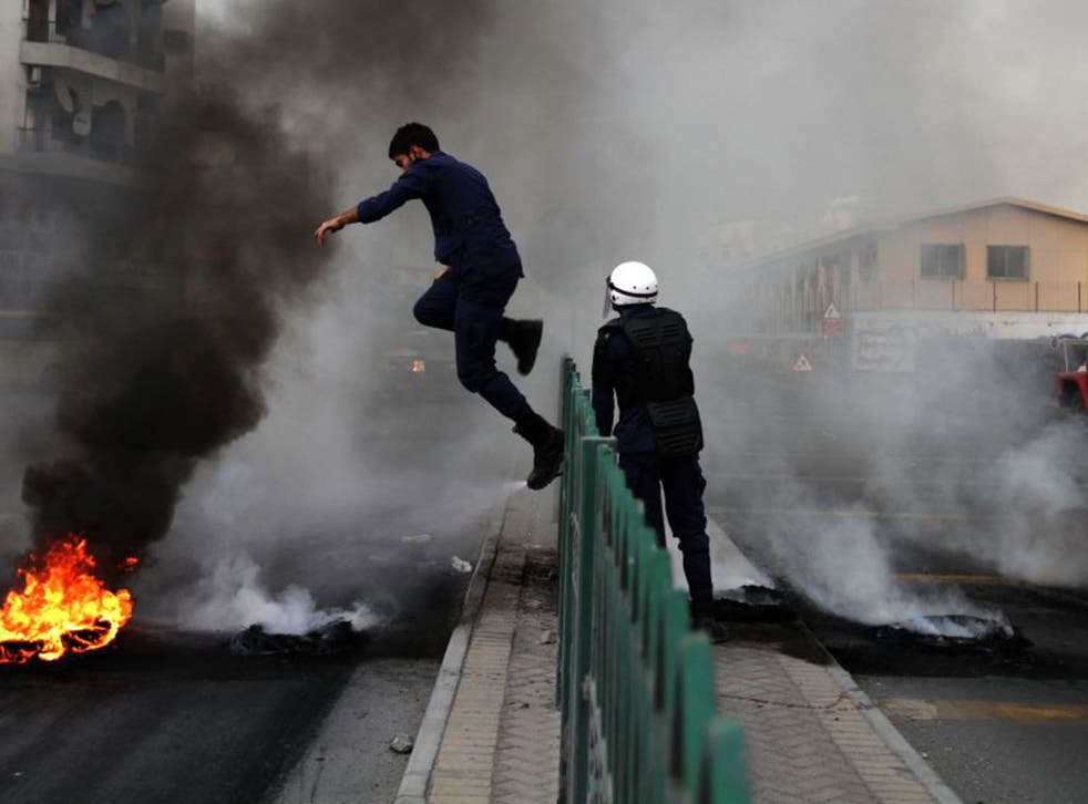 A riot policeman jumps a fence to extinguish a tire fire set by Bahraini anti-government protesters in Sehla