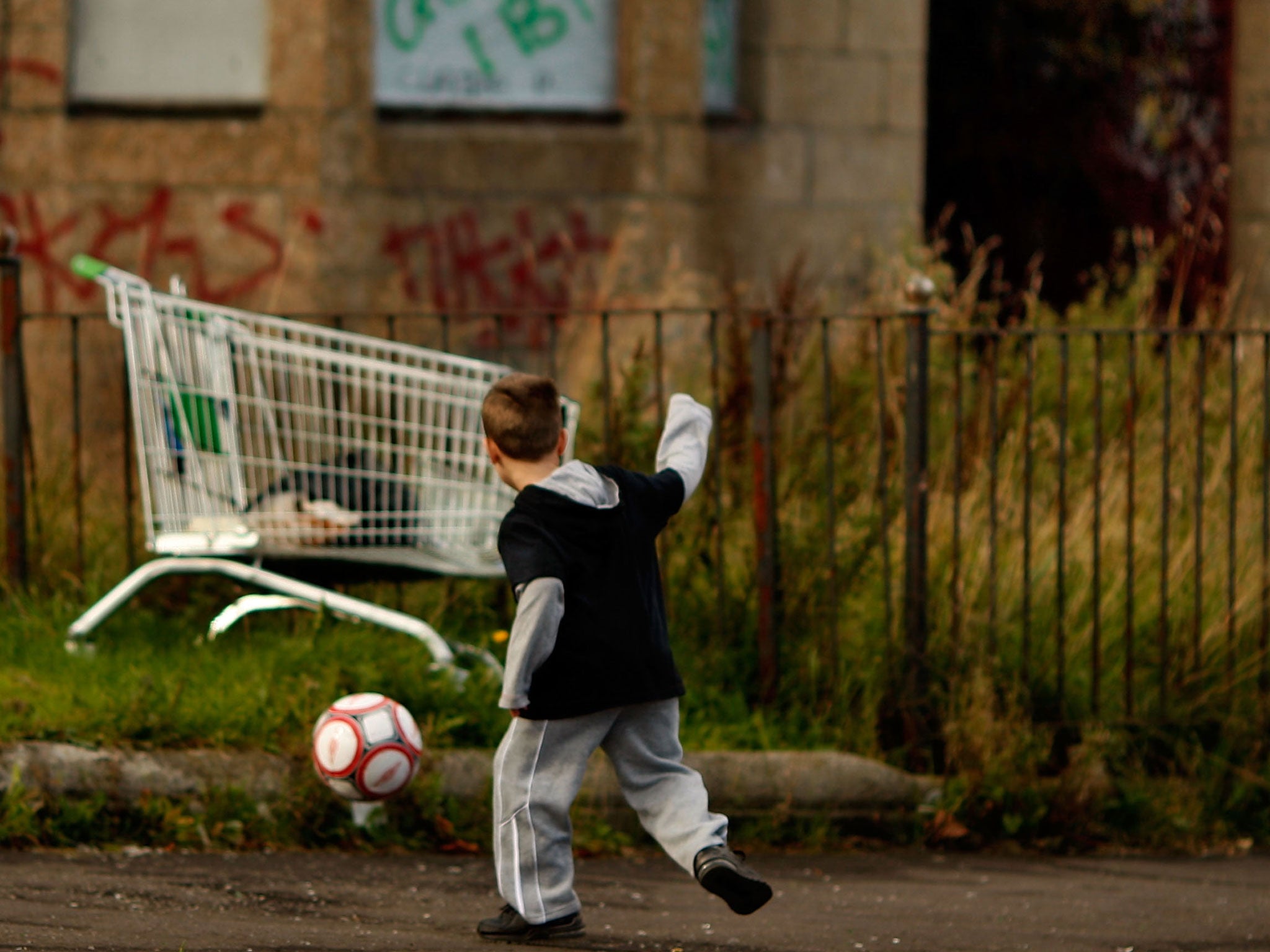 A young boy play's football in a street in Govan