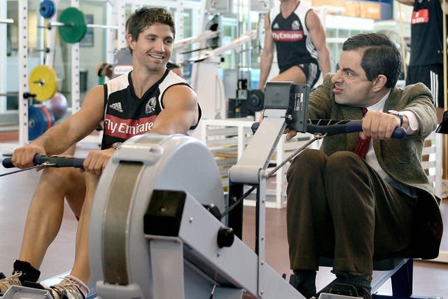 Actor Rowan Atkinson in character as Mr Bean trains on a rowing machine as Brodie Holland of the Magpies looks on during the Collingwood Magpies AFL gym training session at the Lexus Centre on March 9, 2007 in Melbourne, Australia.