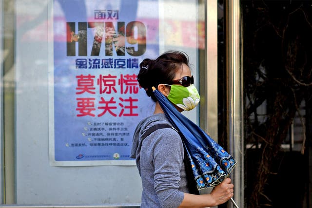 A woman wears a face mask as she walks past a poster in Beijing showing how to avoid getting the H7N9 bird flu virus