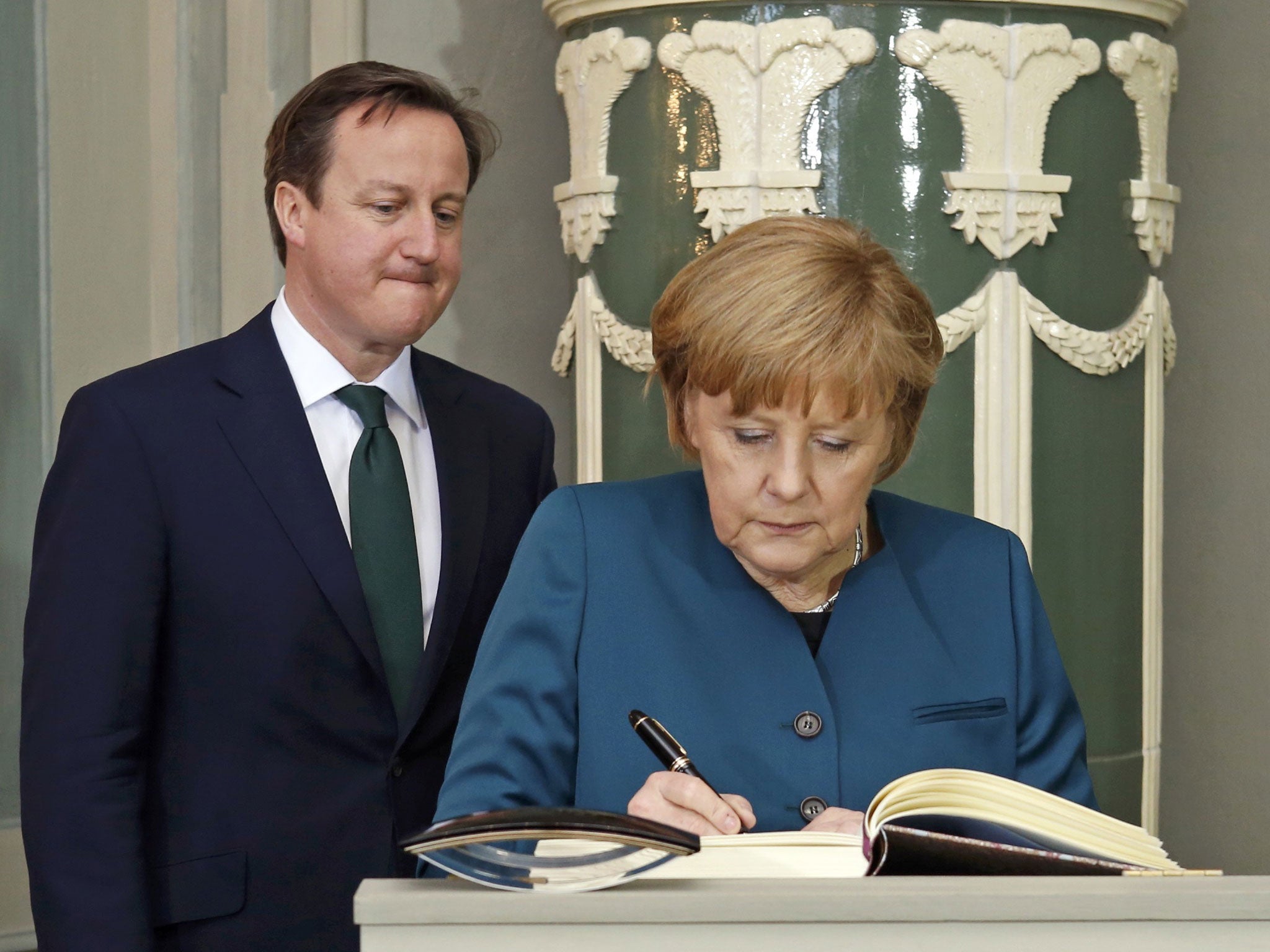 German Chancellor Angela Merkel signs the guestbook as Britain's Prime Minister David Cameron looks on inside the government's guest house Schloss Meseberg, 70 km (44 miles) north of Berlin on April 12, 2013.