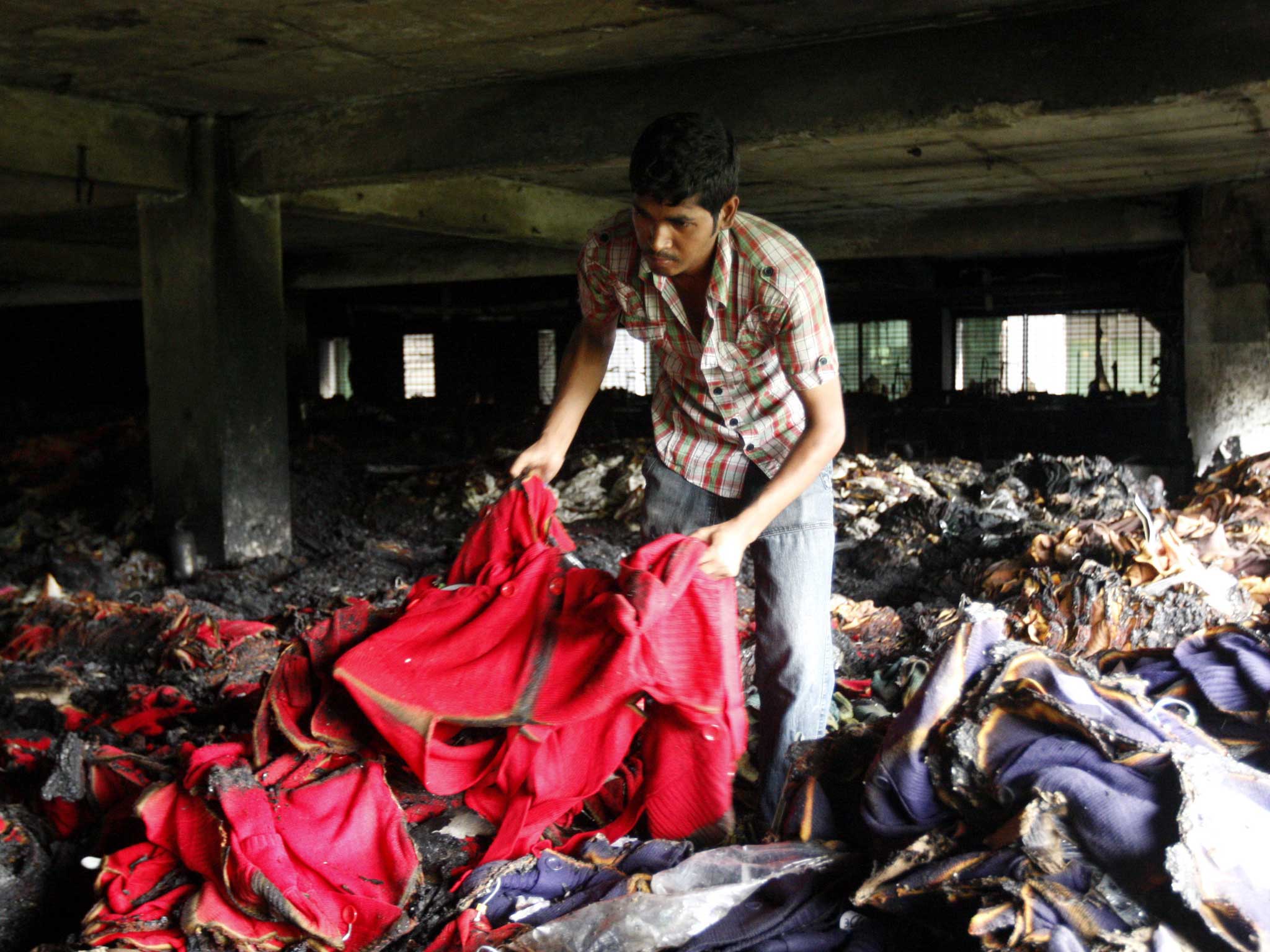A worker inspects burnt sweaters on the second floor of the building of the readymade garment factory after the devastating fire