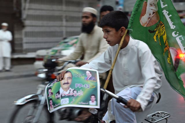 A Pakistani youth rides a bicycle bearing a party flag and poster on a street in Rawalpindi