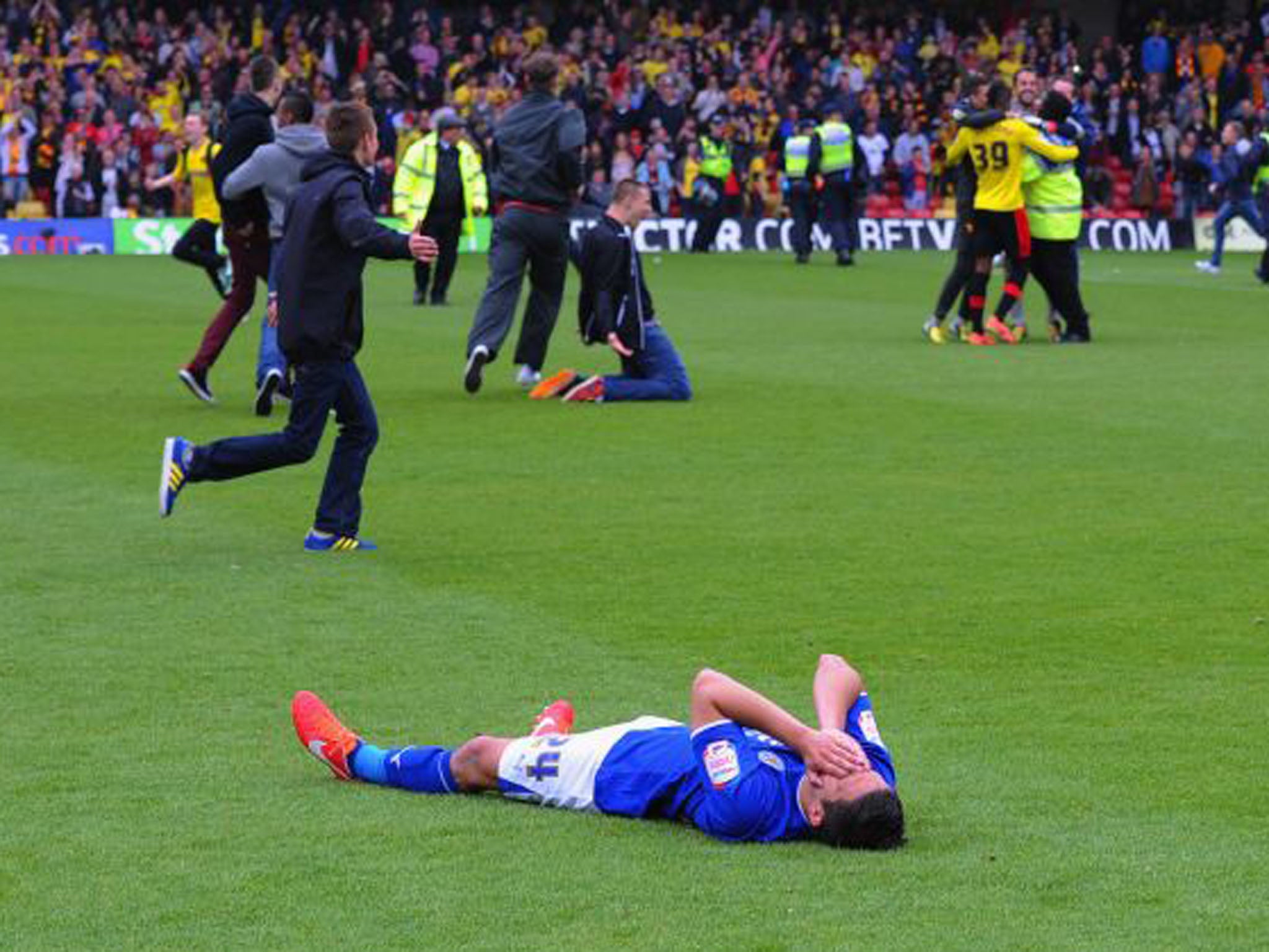 Anthony Knockaert of Leicester lies on the turf after his team's loss to Watford to exit the play-offs, while Watford fans run onto the pitch to celebrate (Michael Regan/Getty Images)