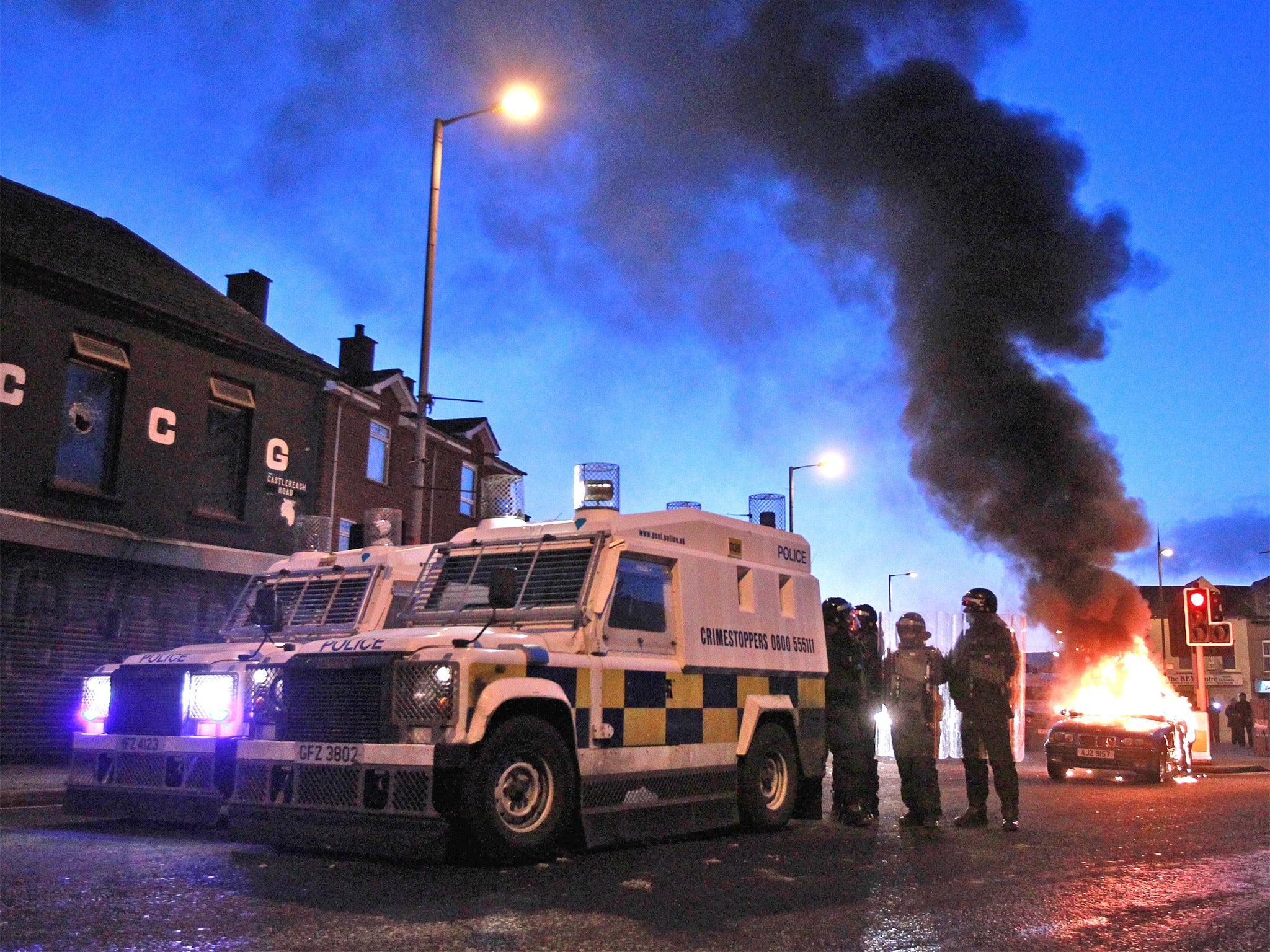 Police stand by their armoured vehicles as a car burns following violence east Belfast in January