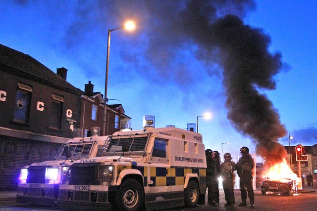 Police stand by their armoured vehicles as a car burns following violence east Belfast in January