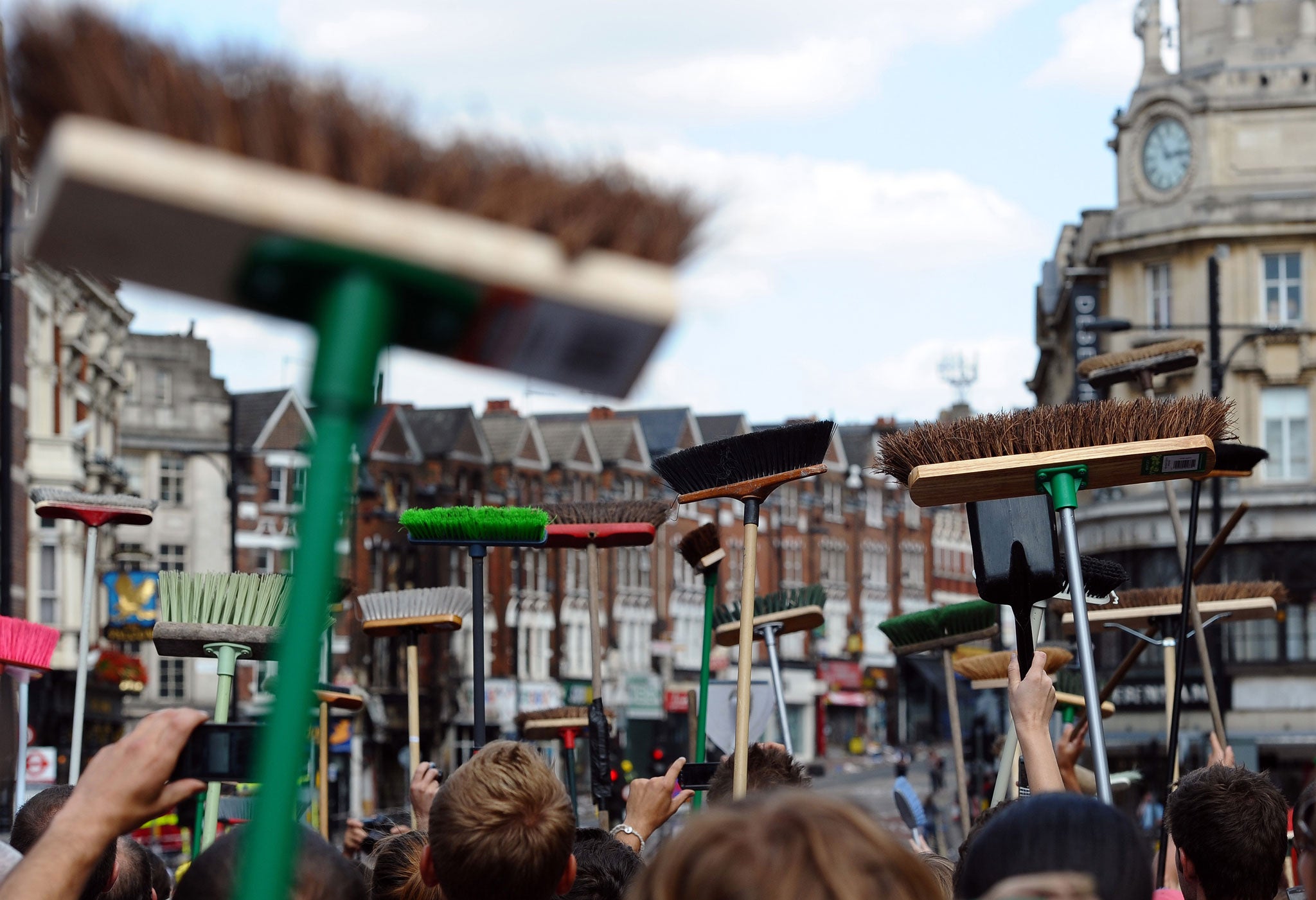 Members of the public show their brushes on August 9, 2011, as they prepare to clean their streets in Clapham Junction, in south London, after riots hit the area