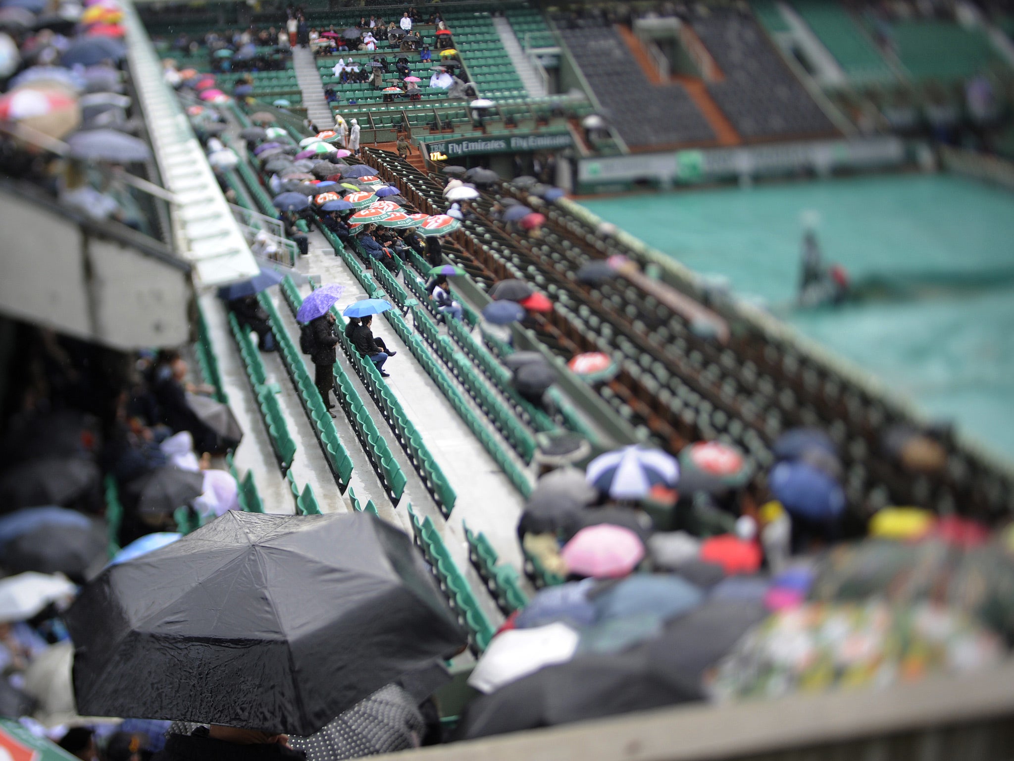 People wait on the Philippe Chatrier central court as rain stops play on day five of the French