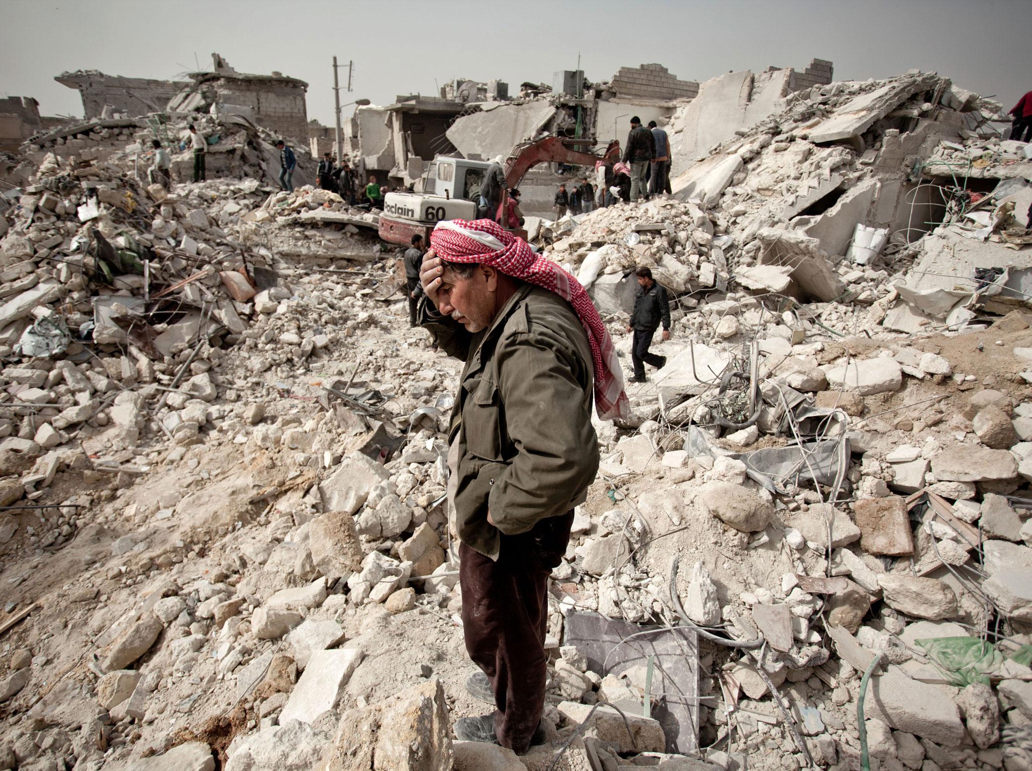 A Syrian man reacts while standing on the rubble of his house while others look for survivors and bodies in the Tariq al-Bab district of the northern city of Aleppo on February 23, 2013.