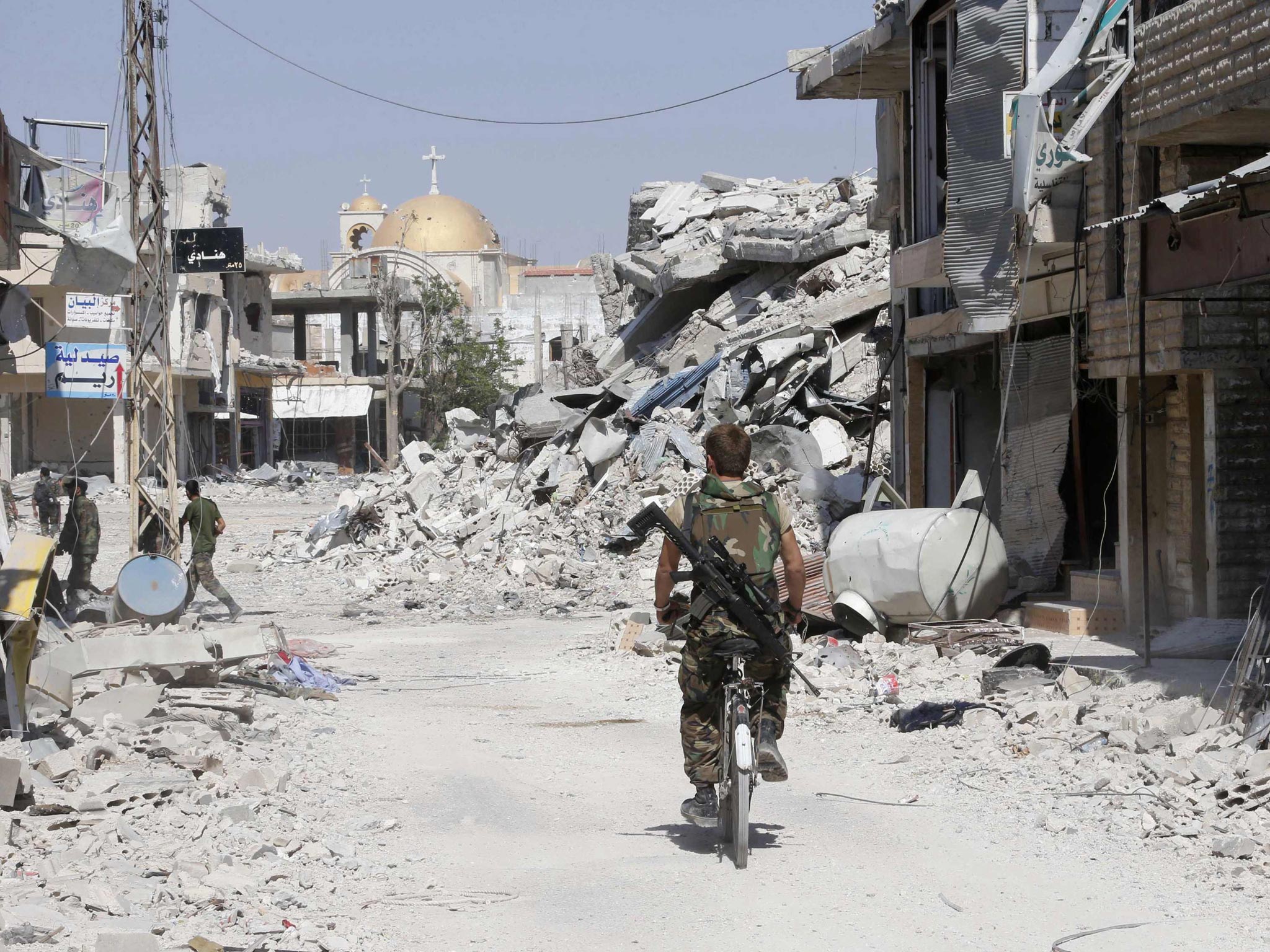 A member of the forces loyal to Syria's President Bashar al-Assad rides a bike along a street piled with damaged buildings in Qusayr, after the Syrian army took control of the city from rebel fighters