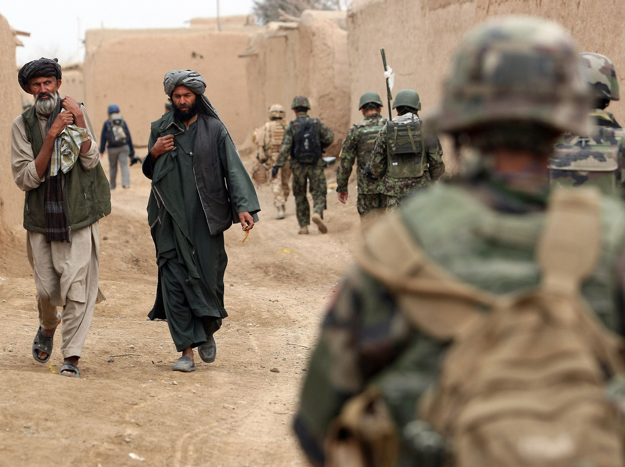 Afghan men walk past a patrol conducted by British soldiers of the 1st batallion of the Royal Welsh, French soldiers of the 21st RIMA and Afghan soldiers in a street of the city of Showal in Nad-e-Ali district, Southern Afghanistan, in Helmand province on February 25, 2010.