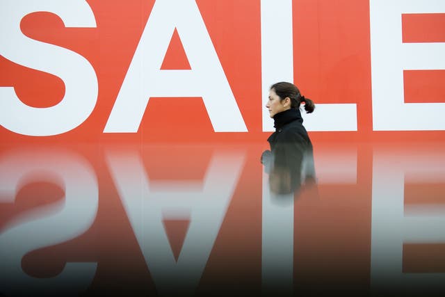 A picture taken using a pre-positioned reflective surface to produce the reflection shows a woman passing a sign advertising an in-store sale in central London on December 16, 2012, less than two weeks before Christmas.