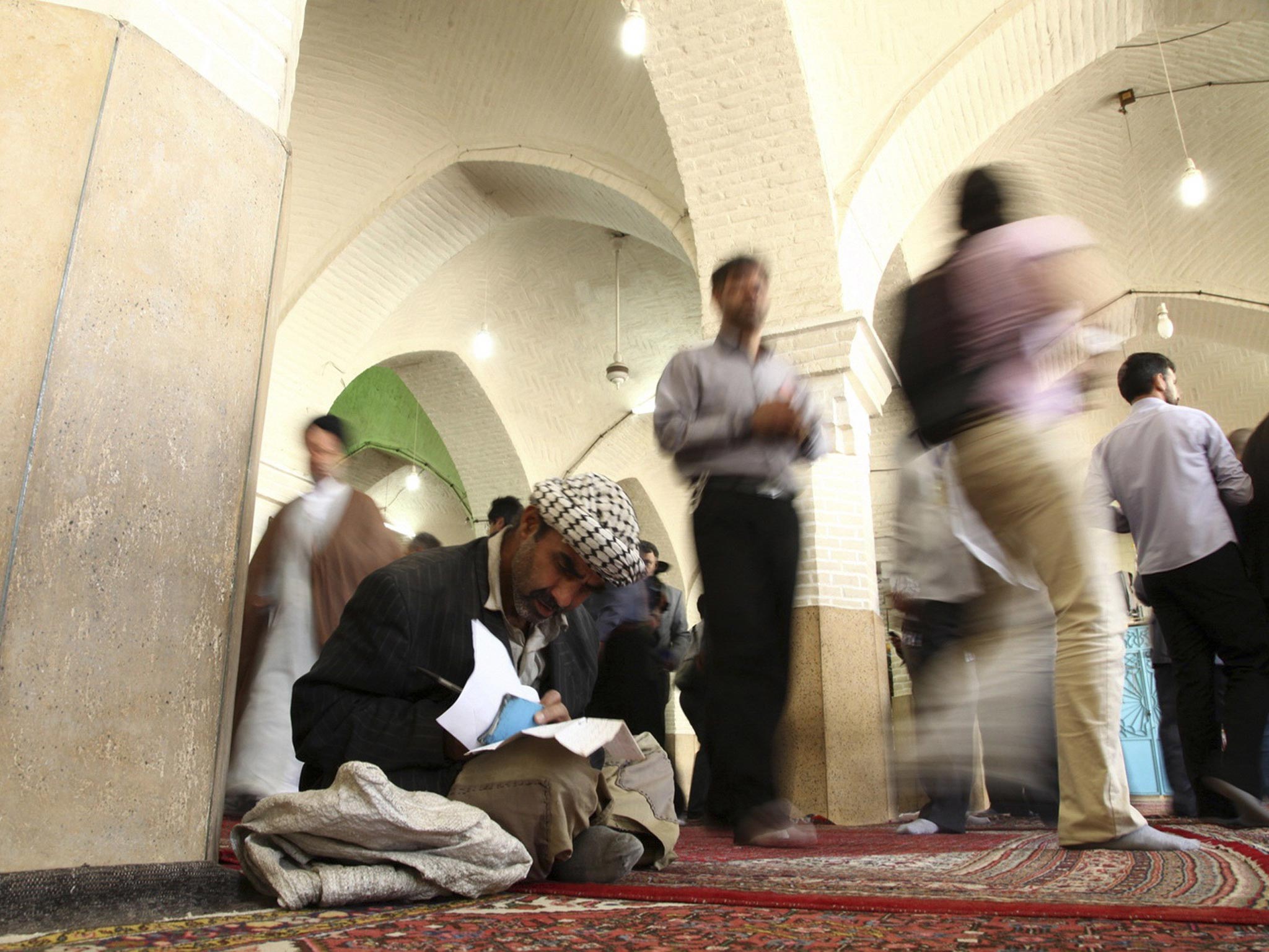A man sits on the ground as he fills in his ballot paper during the Iranian presidential election at a mosque in Qom, Iran
