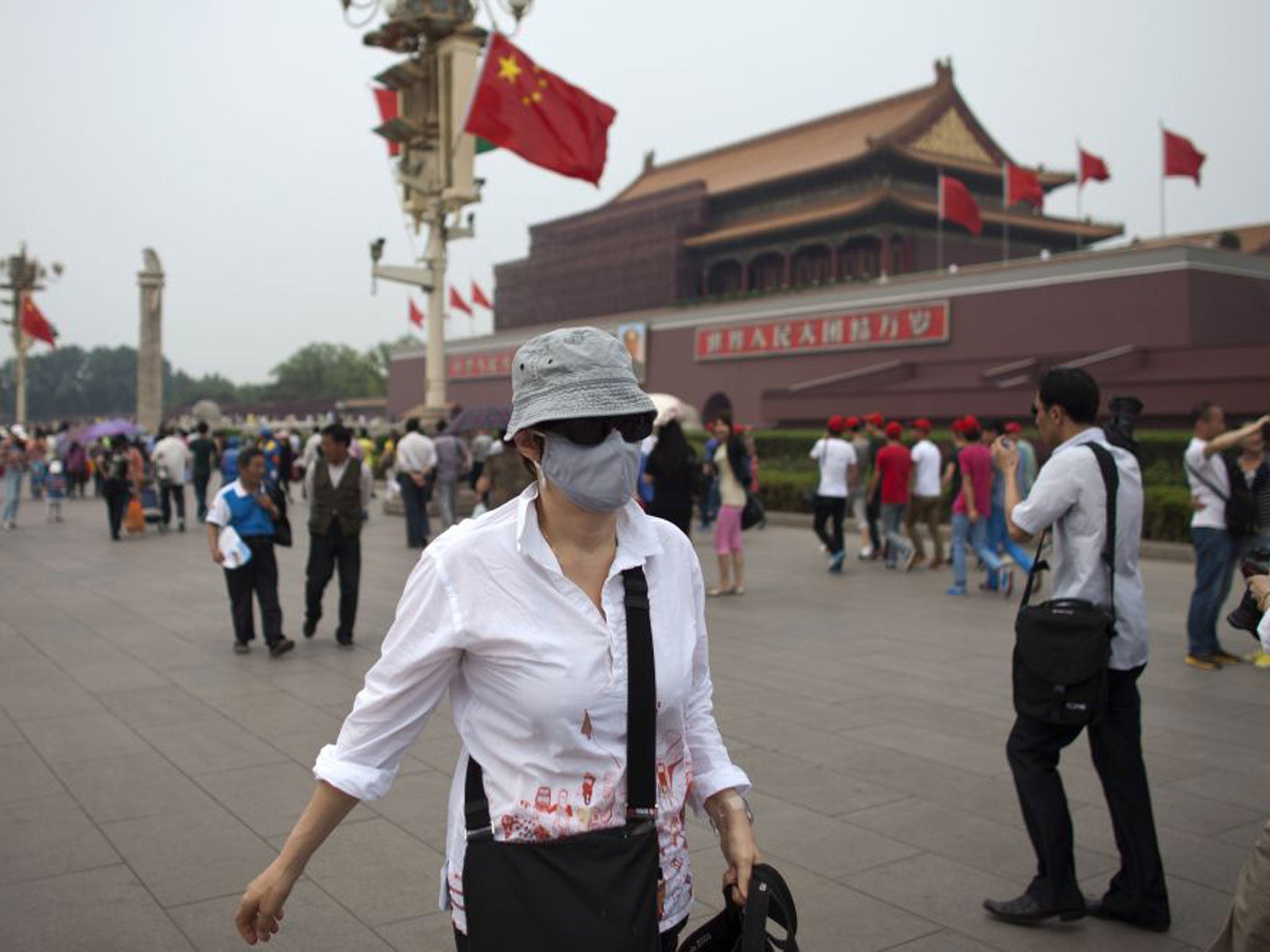 A foreign tourist wearing a mask walks in front of Tiananmen Gate on a polluted day in Beijing