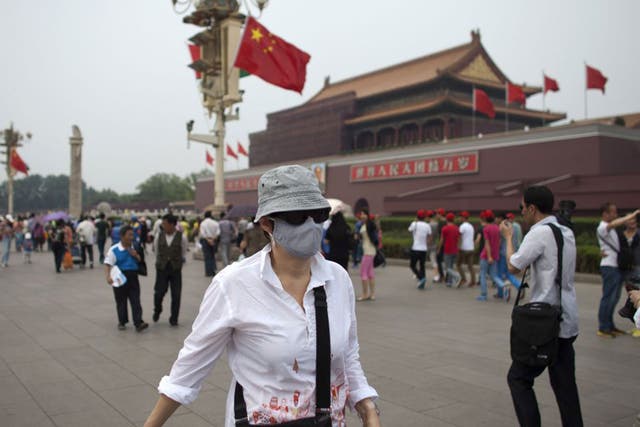 A foreign tourist wearing a mask walks in front of Tiananmen Gate on a polluted day in Beijing