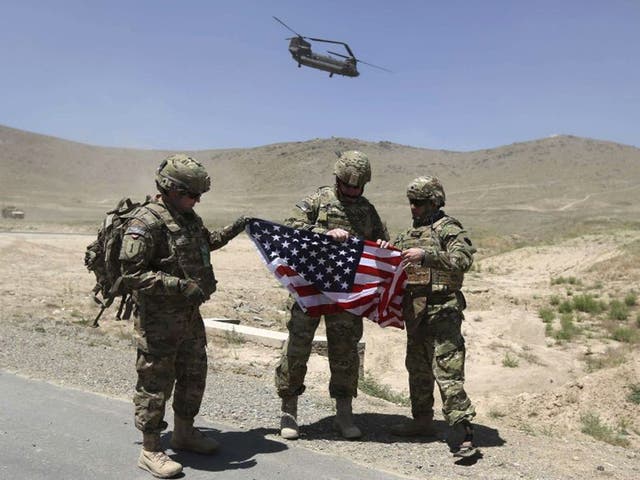 Nato soldiers stand with US flag as a Chinook helicopter takes off after a security handover ceremony at a military academy outside Kabul