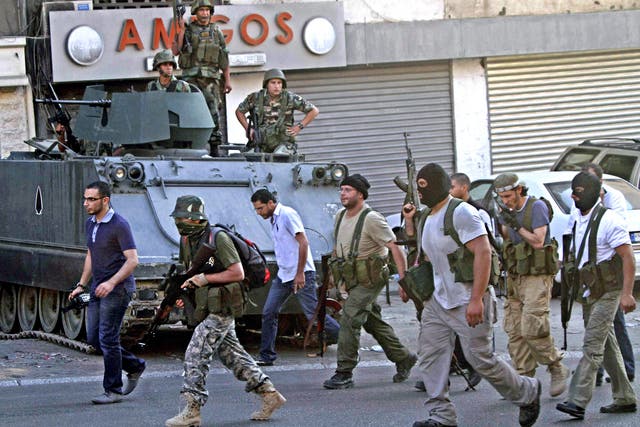 Gunmen and followers of hardline Sunni cleric Sheik Ahmad al-Assir pass in front of Lebanese army soldiers in the southern port city of Sidon