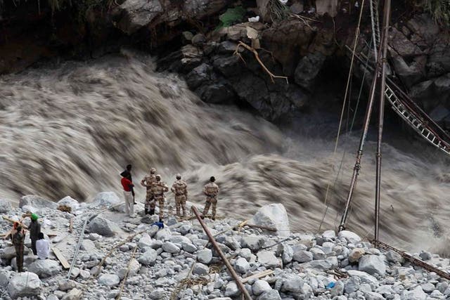 Water gushes down a river as Indian paramilitary soldiers and volunteers stand near a makeshift bridge