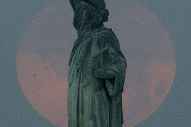 A supermoon sets behind the Statue of Liberty