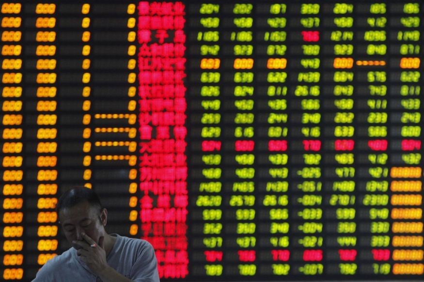An investor smokes in front of an electronic board showing stock information at a brokerage house in Shanghai
