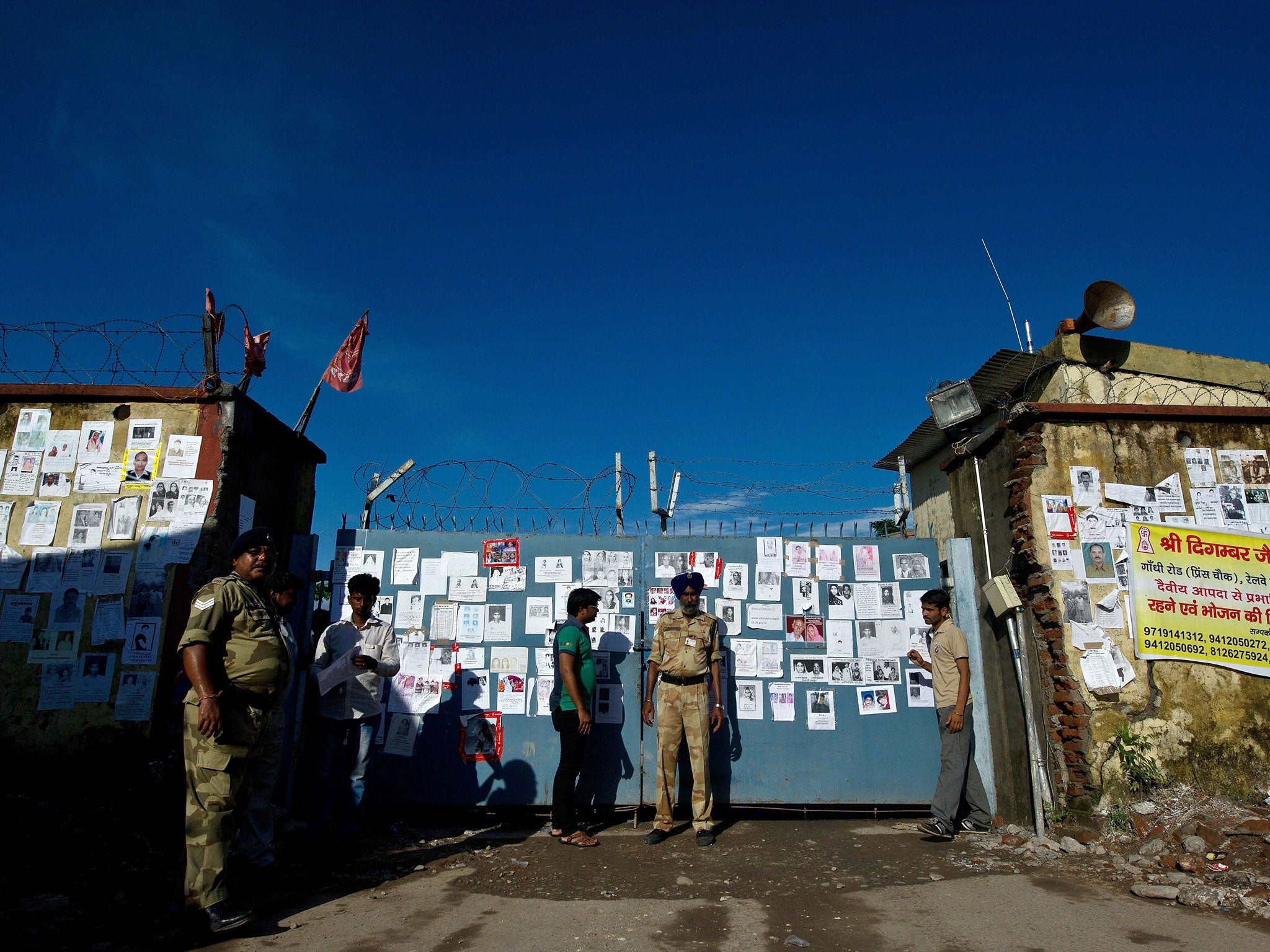 Indian security personnel stand guard at an entrance gate - covered with portraits of missing pilgrims - of the Jolly Grant Airport in Dehradun