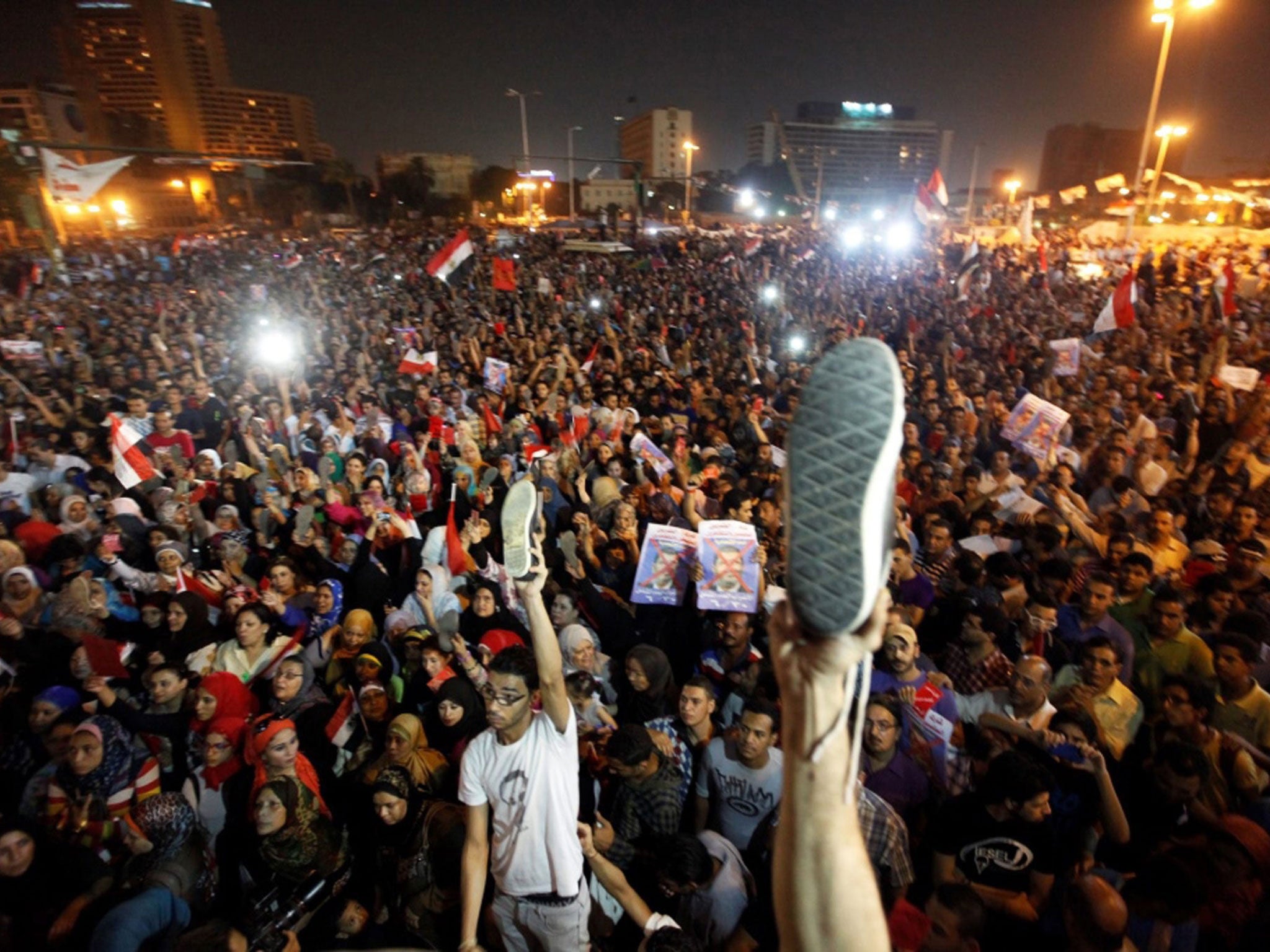 Egyptian opponents of President Mohammed Morsi hold up posters depicting him and their shoes in the air to show their anger, as they listen to his speech during a protest at Tahrir square