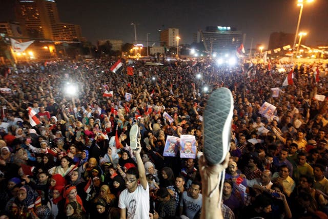 Egyptian opponents of President Mohammed Morsi hold up posters depicting him and their shoes in the air to show their anger, as they listen to his speech during a protest at Tahrir square
