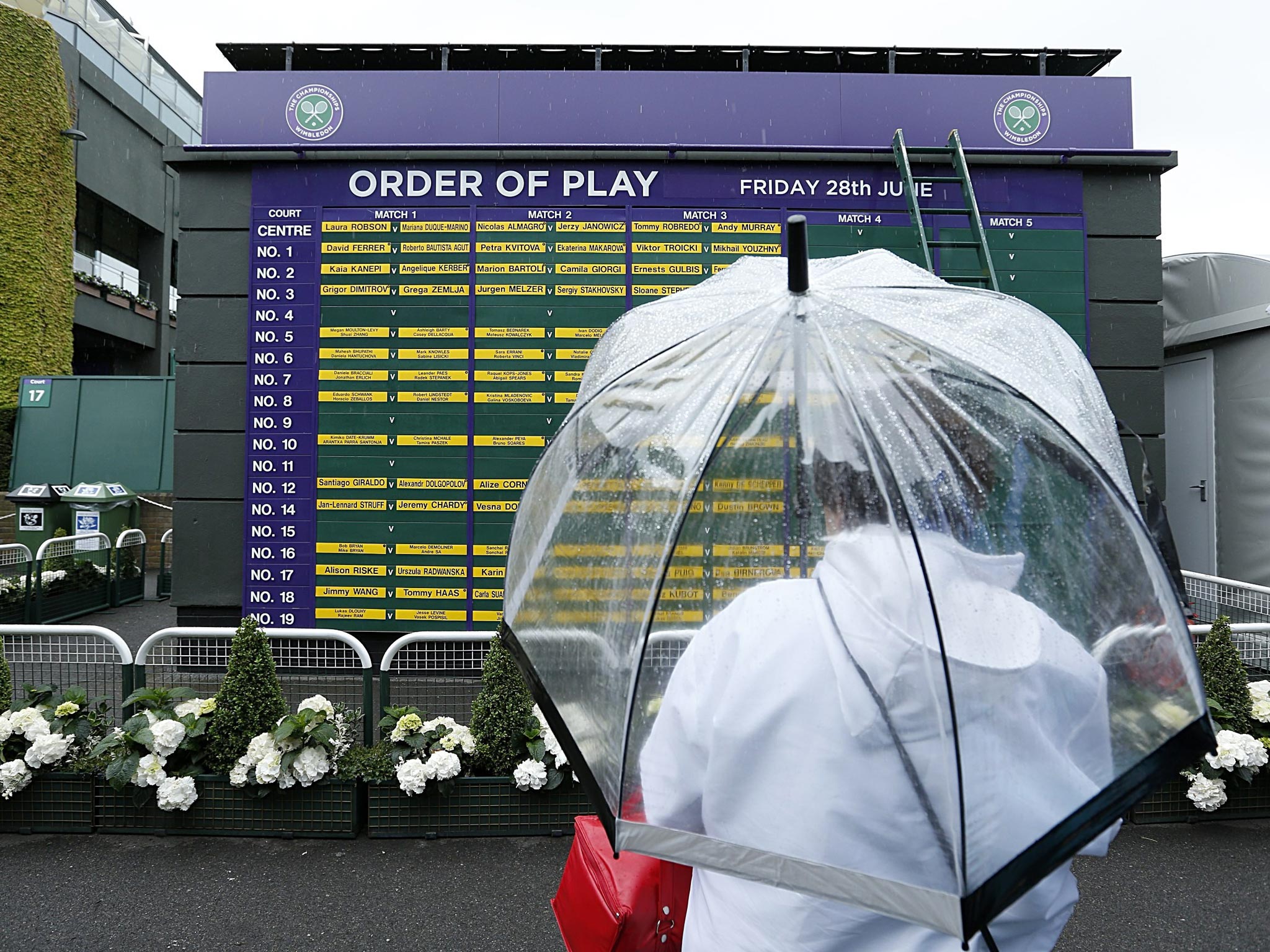 28 June 2013: A fan checks the days order of play under an umbrella during day five of the Wimbledon