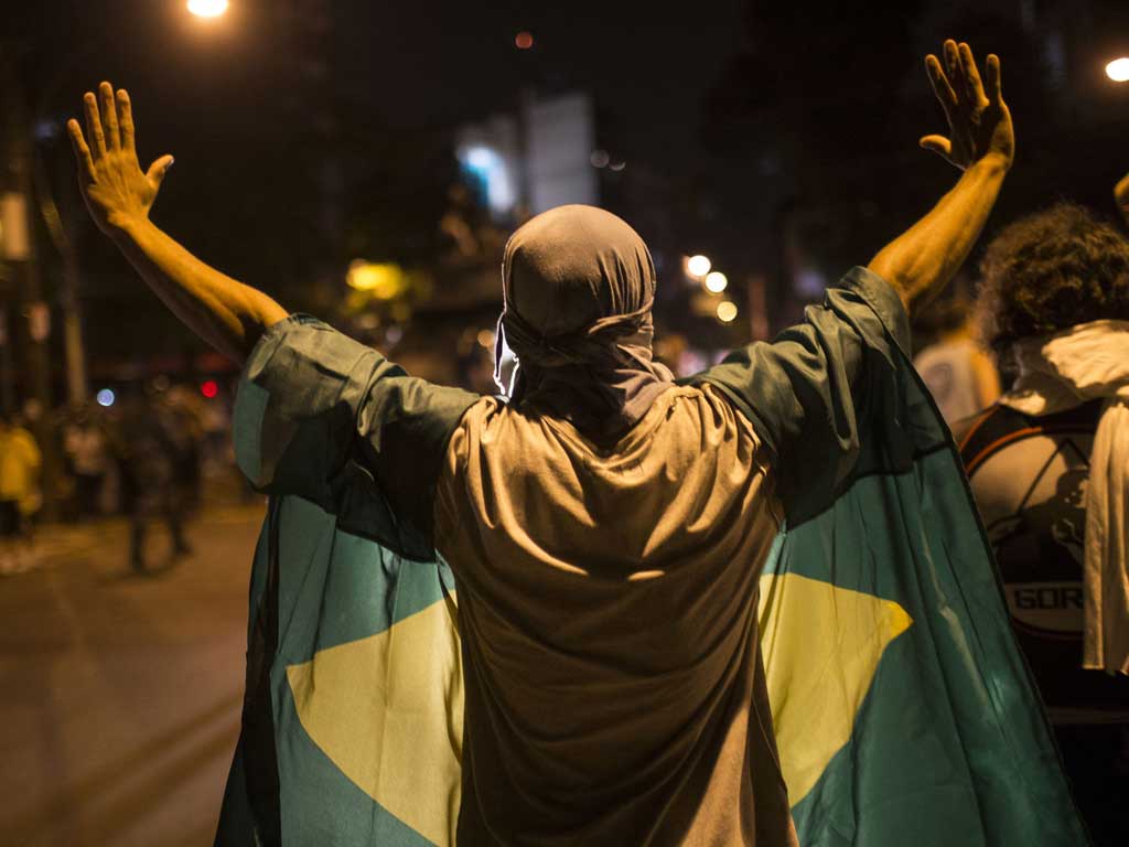 A protester wearing a brazilian flag hold his hands up as he faces police officers near the Maracana stadium in Rio