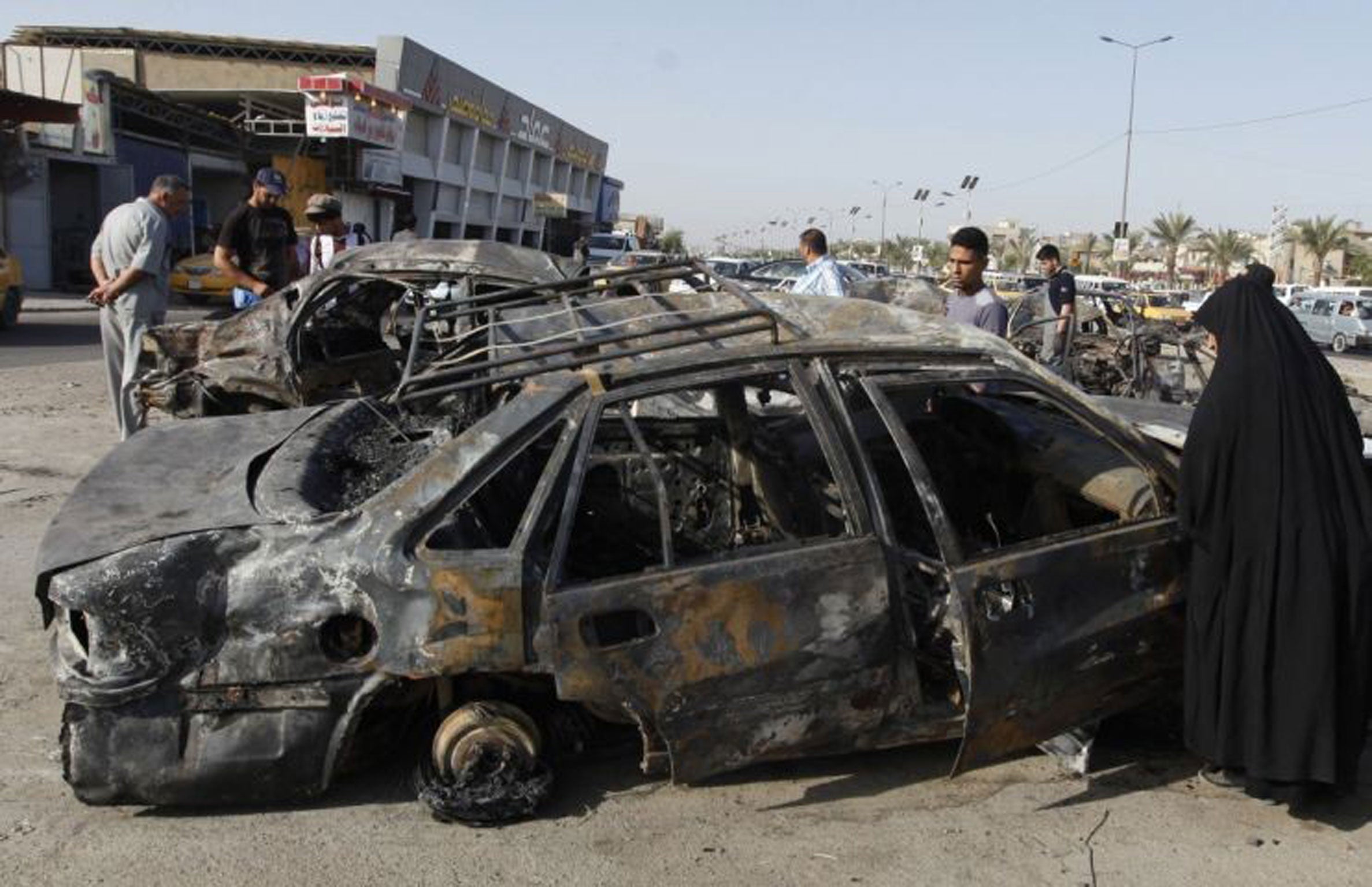 A woman looks over the remains of a car after 45 were killed in Baghdad in a series of car bomb attacks on Tuesday