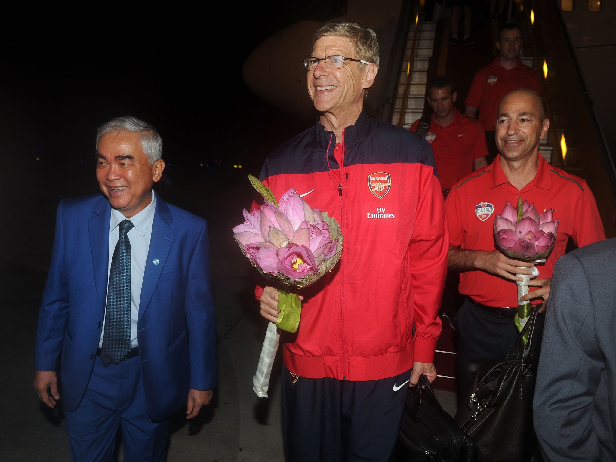 Arsene Wenger (c) and Ivan Gazidis (r) are greeted as they arrive in Vietnam