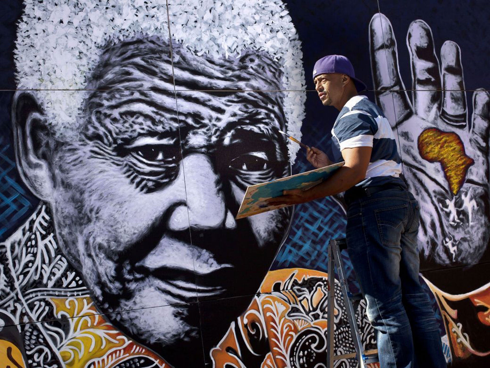 The artist John Adams puts the finishing touches to a giant acrylic on canvas painting of Nelson Mandela outside his house in a suburb of Johannesburg on Monday