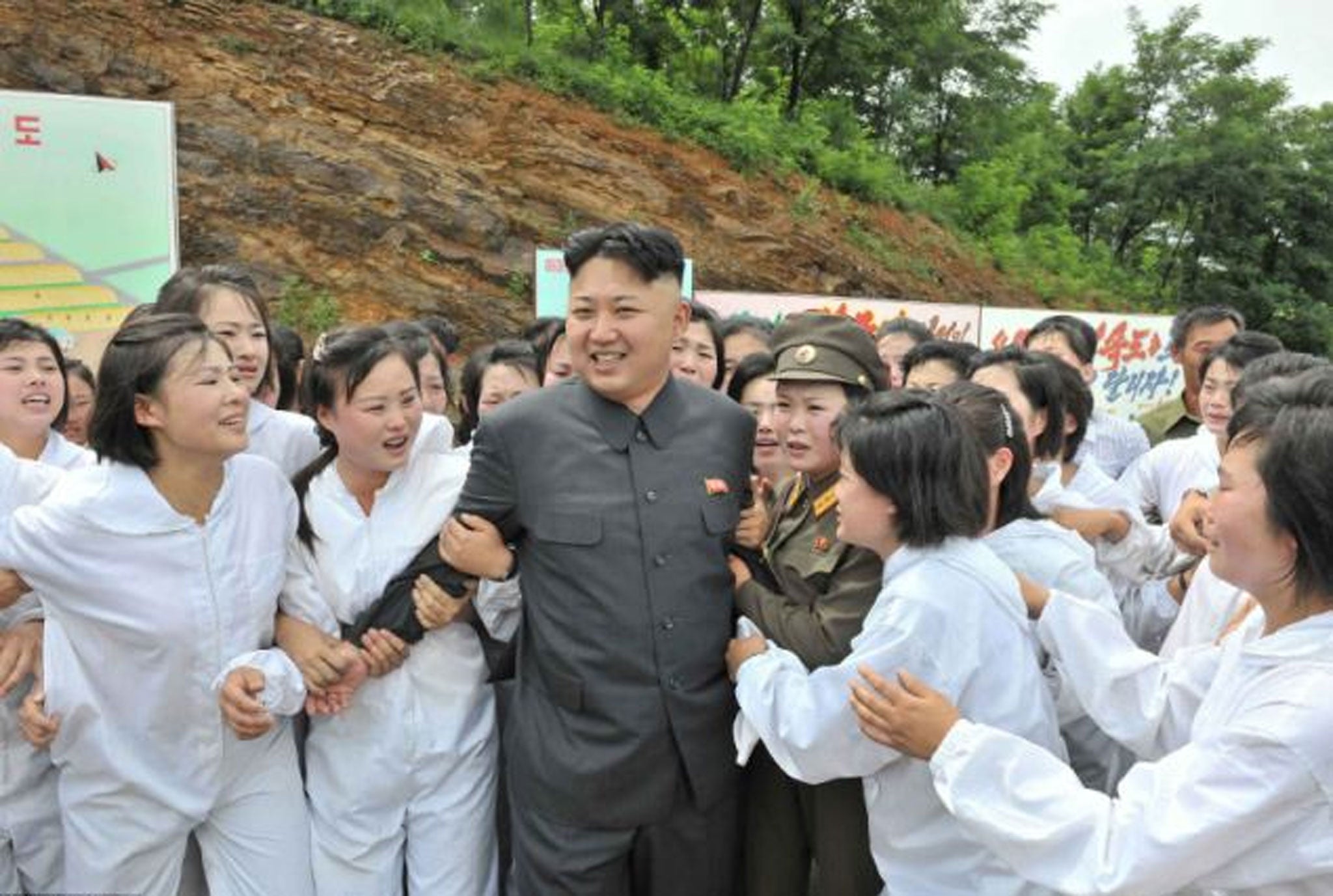 A smiling Kim Jong-un is seen being mobbed by a large group of crying women wearing white boiler suits